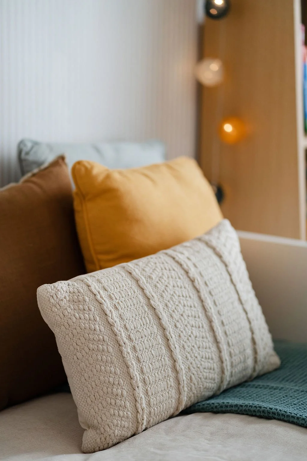 Imagem de almofadas de diferentes cores e texturas em um sofá, com iluminação suave ao fundo.