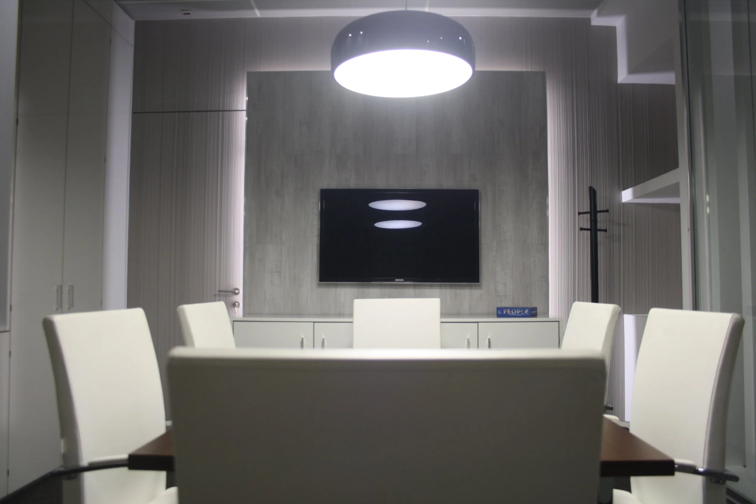 Sala de reuniões com painel retroiluminado, candeeiros de teto e cadeiras estofadas a pele branca