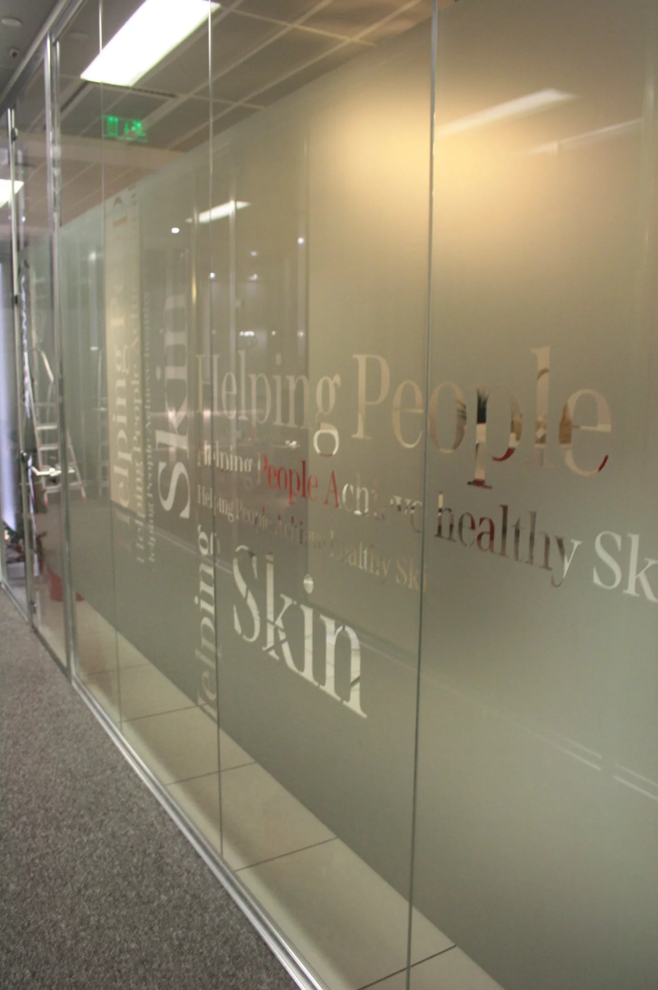 Corredor com divisória em vidro, decorada a vinil frost com lettering recortado.