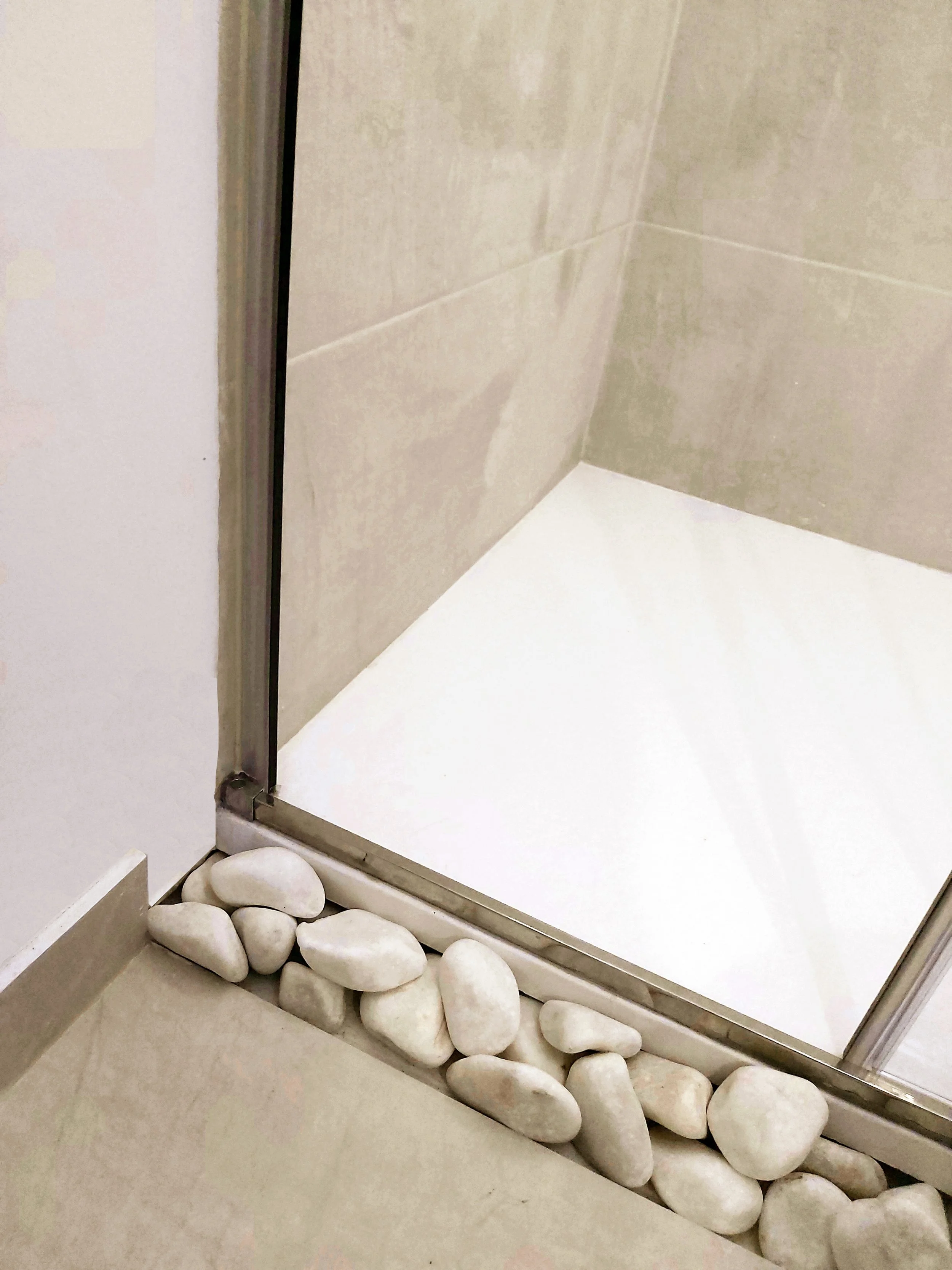 Chão e parede de banheiro, com pedras brancas decorativas na base do box de vidro.