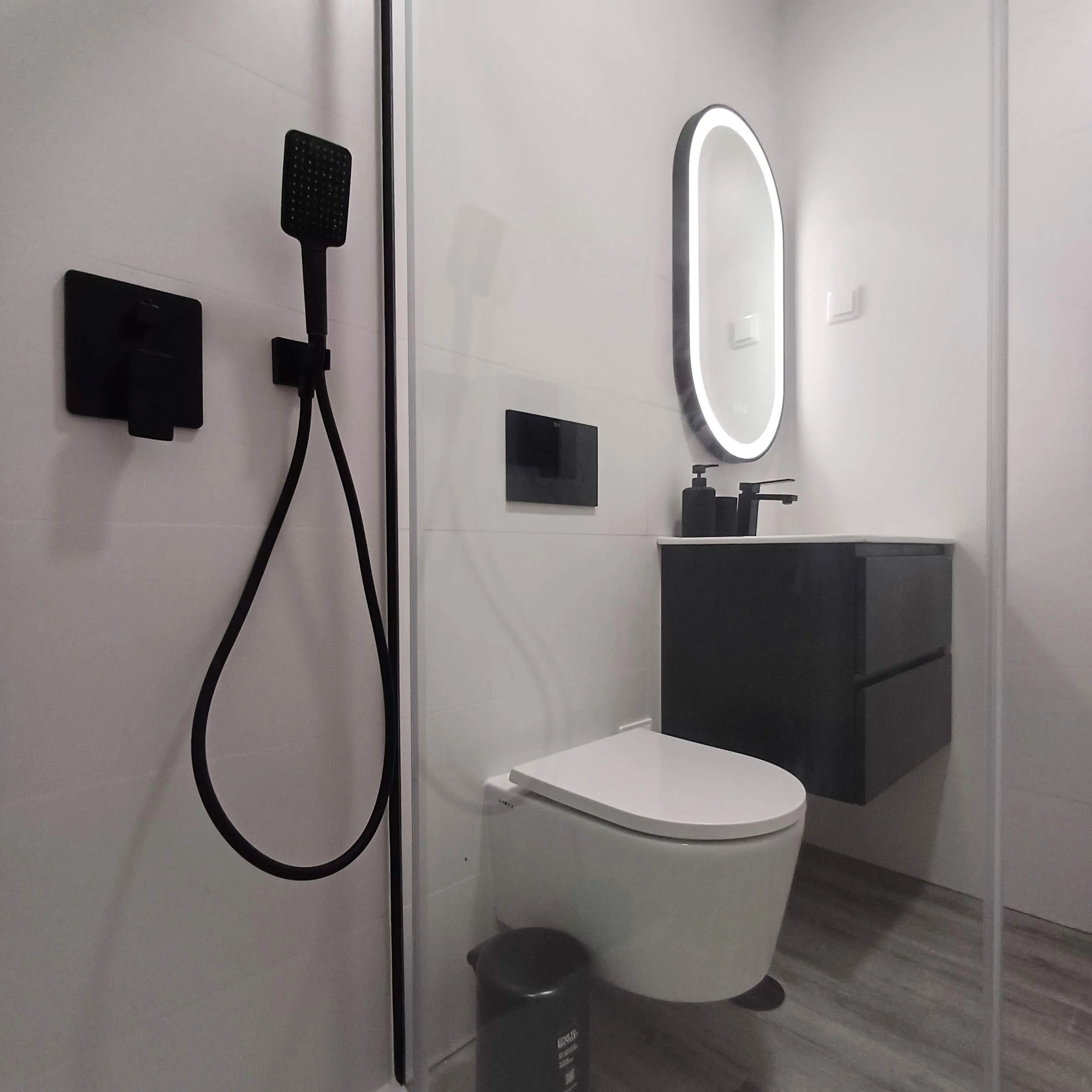 Decoração de Apartamento no Parque das Nações, Lisboa. Casa-de-Banho com  Decoração Preto/Branco, iluminação LED, combinado de duche de encastre, acessórios de cor preta e pavimento vinílico acabamento madeira.