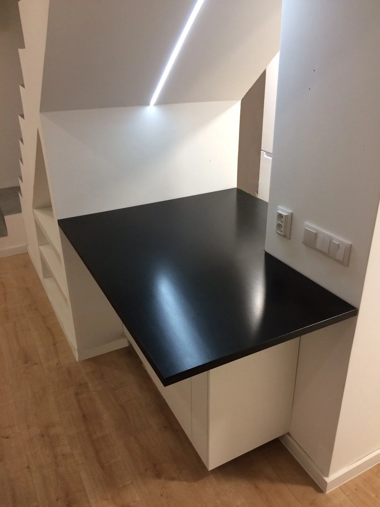 Gabinete com bancada preta e paredes brancas, com tomada elétrica ao lado.