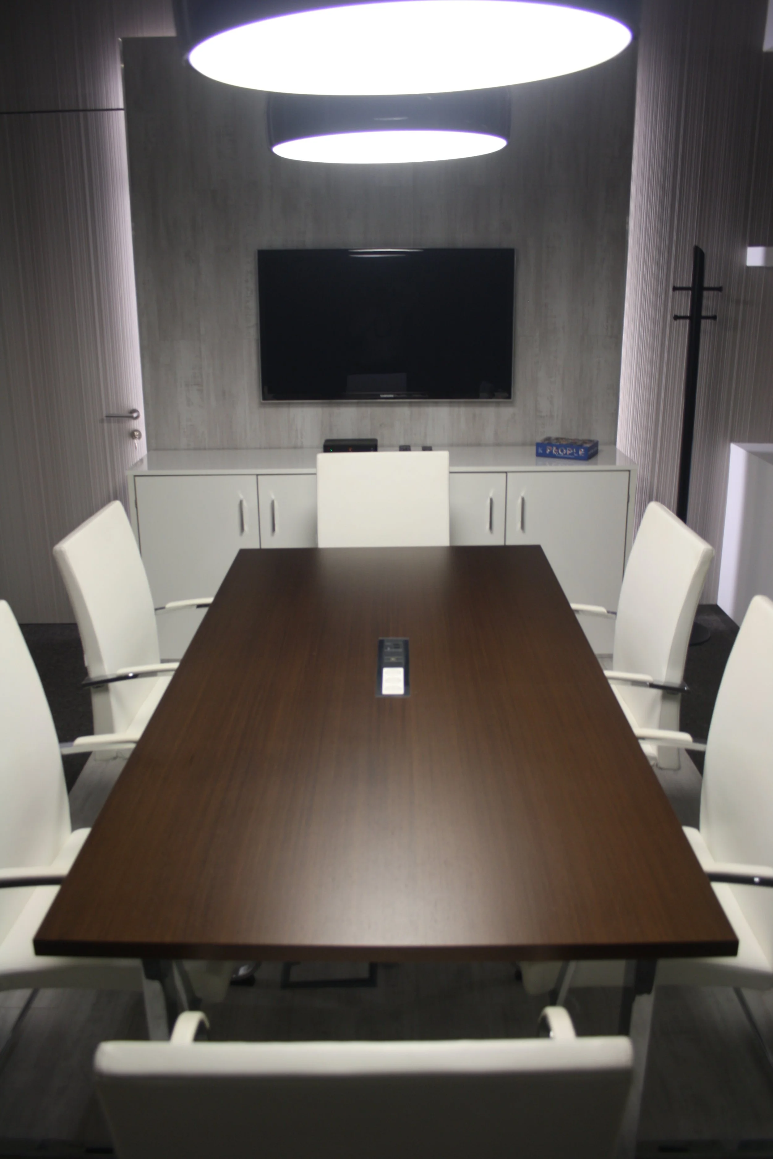 Sala de reuniões com painel retroiluminado, candeeiros de teto e cadeiras estofadas a pele branca.