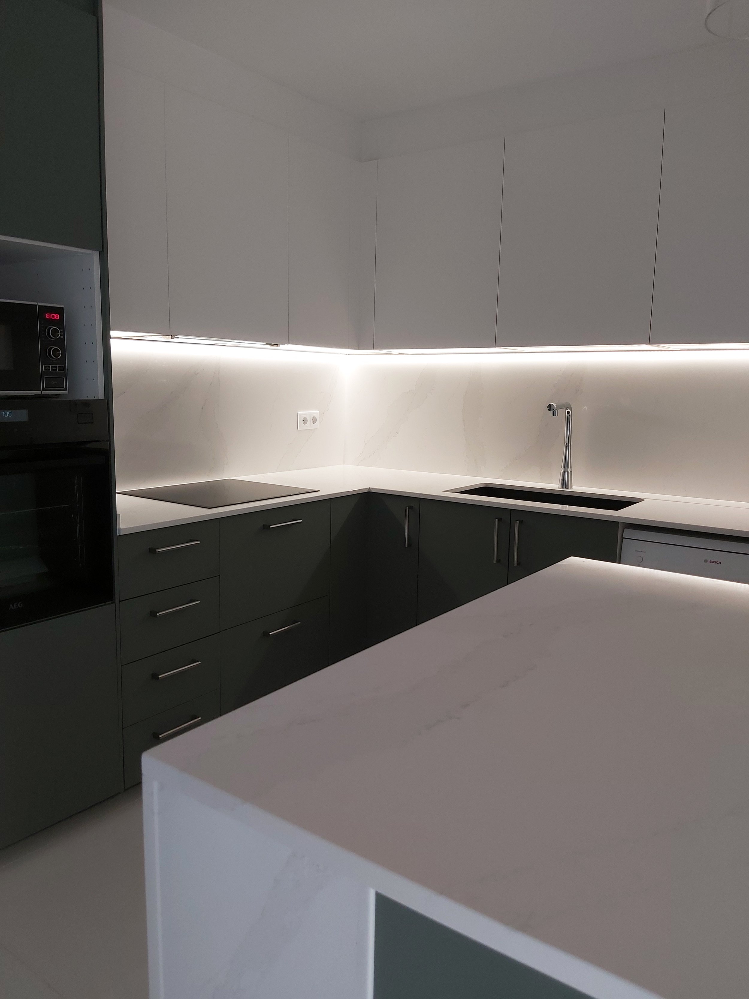 Cozinha com península e tampos e backsplash em silstone calacatta gold. Iluminação suspensa e indireta