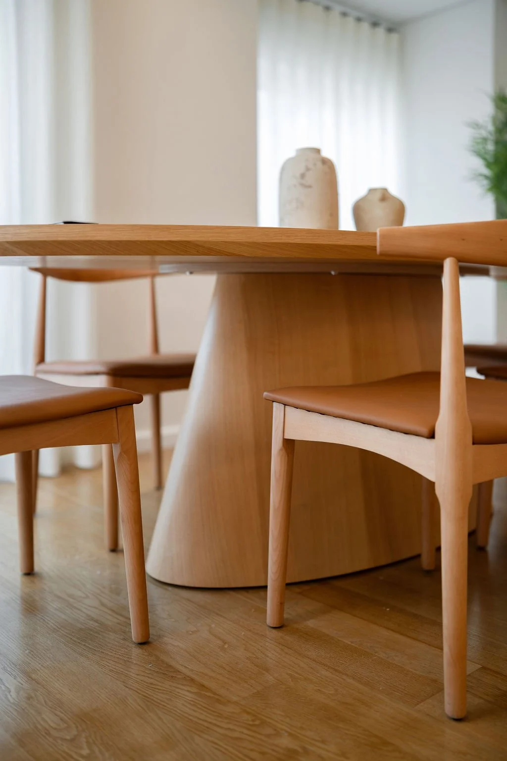 Sala de jantar minimalista com mesa de madeira oval, seis cadeiras de madeira com assentos em pele sintética.