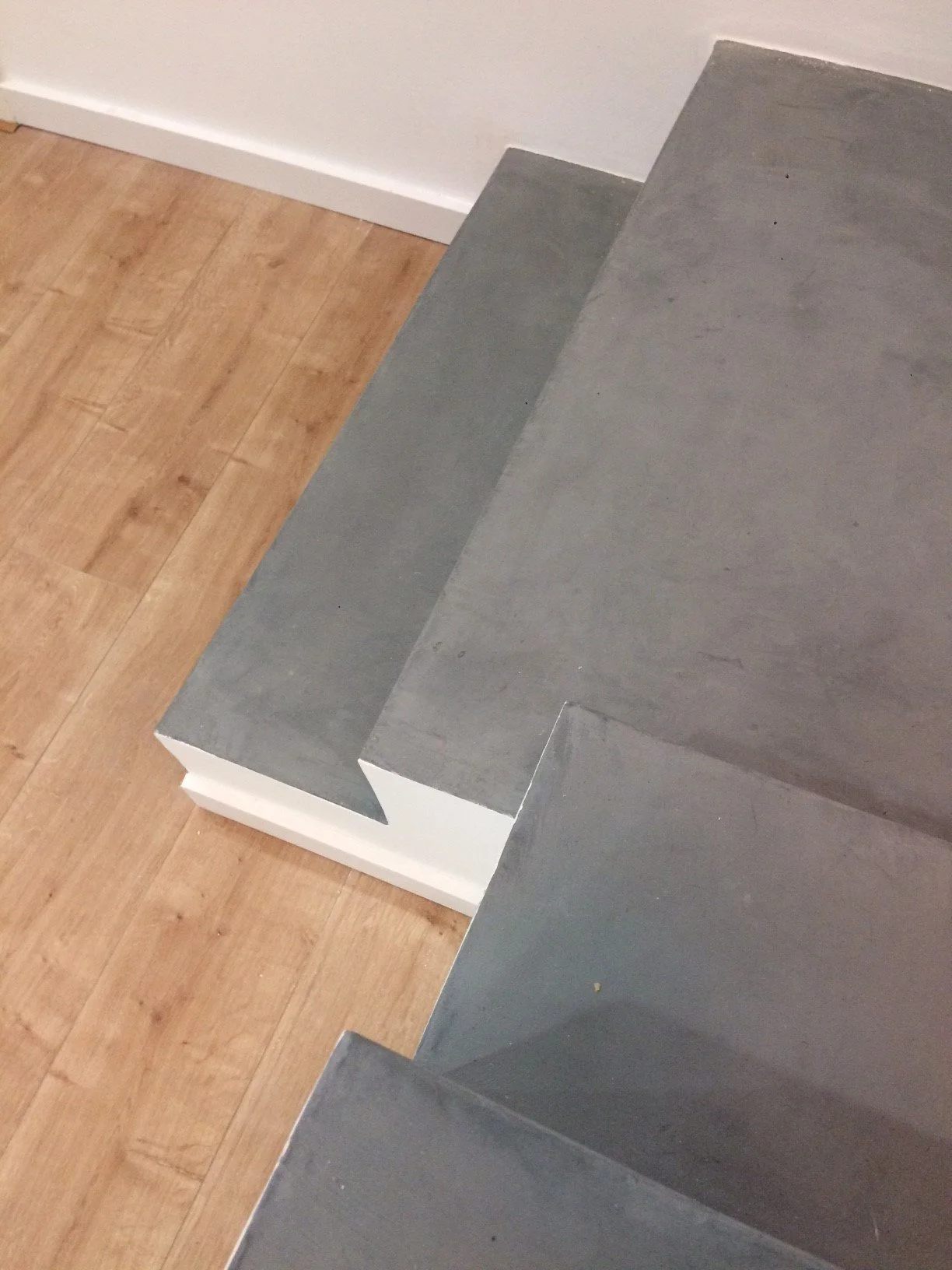 Imagem de uma escada de degraus de cimento cinza, com piso de madeira ao lado.