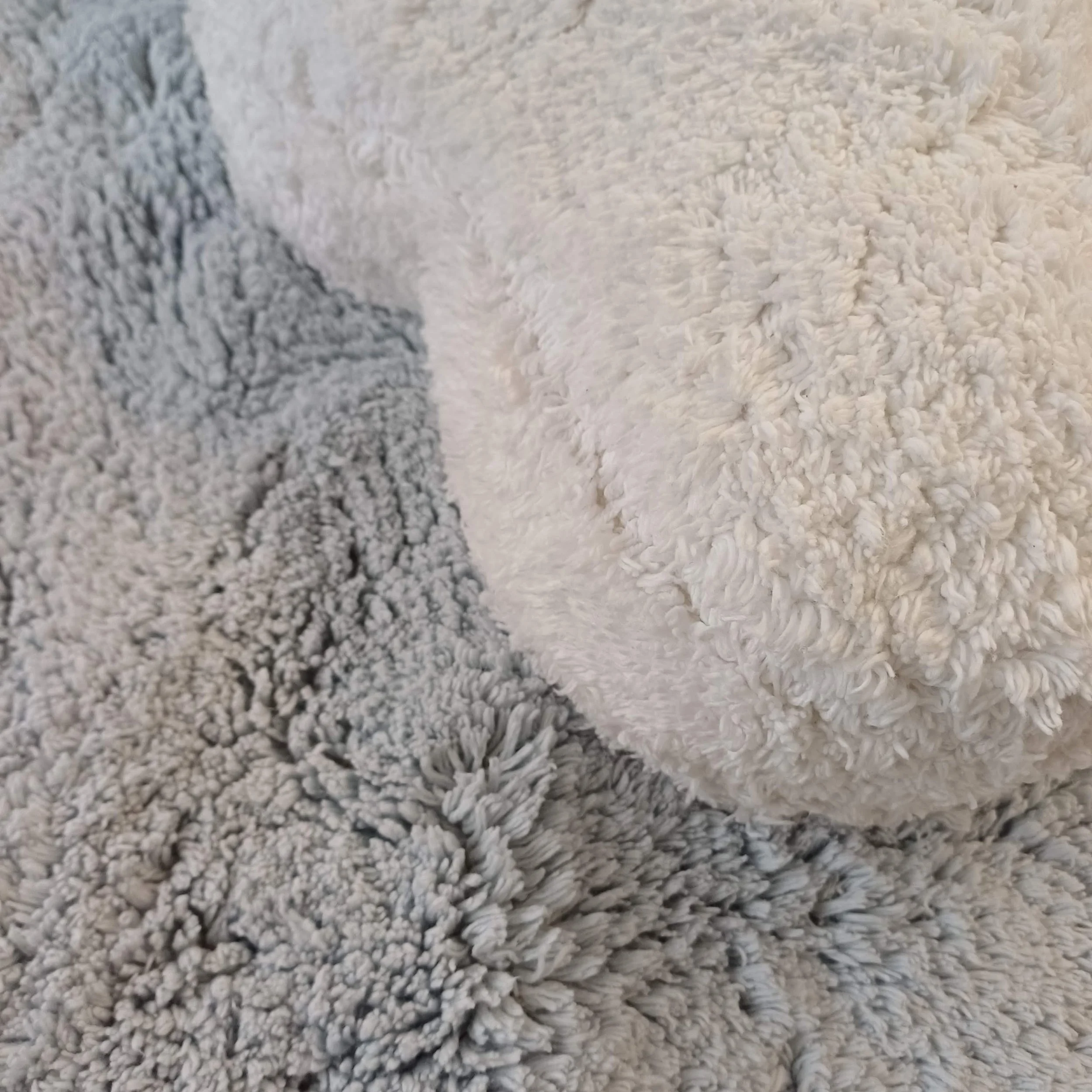 Três almofadas de pelúcia, uma branca e duas cinza, colocadas sobre uma manta de pelúcia cinza