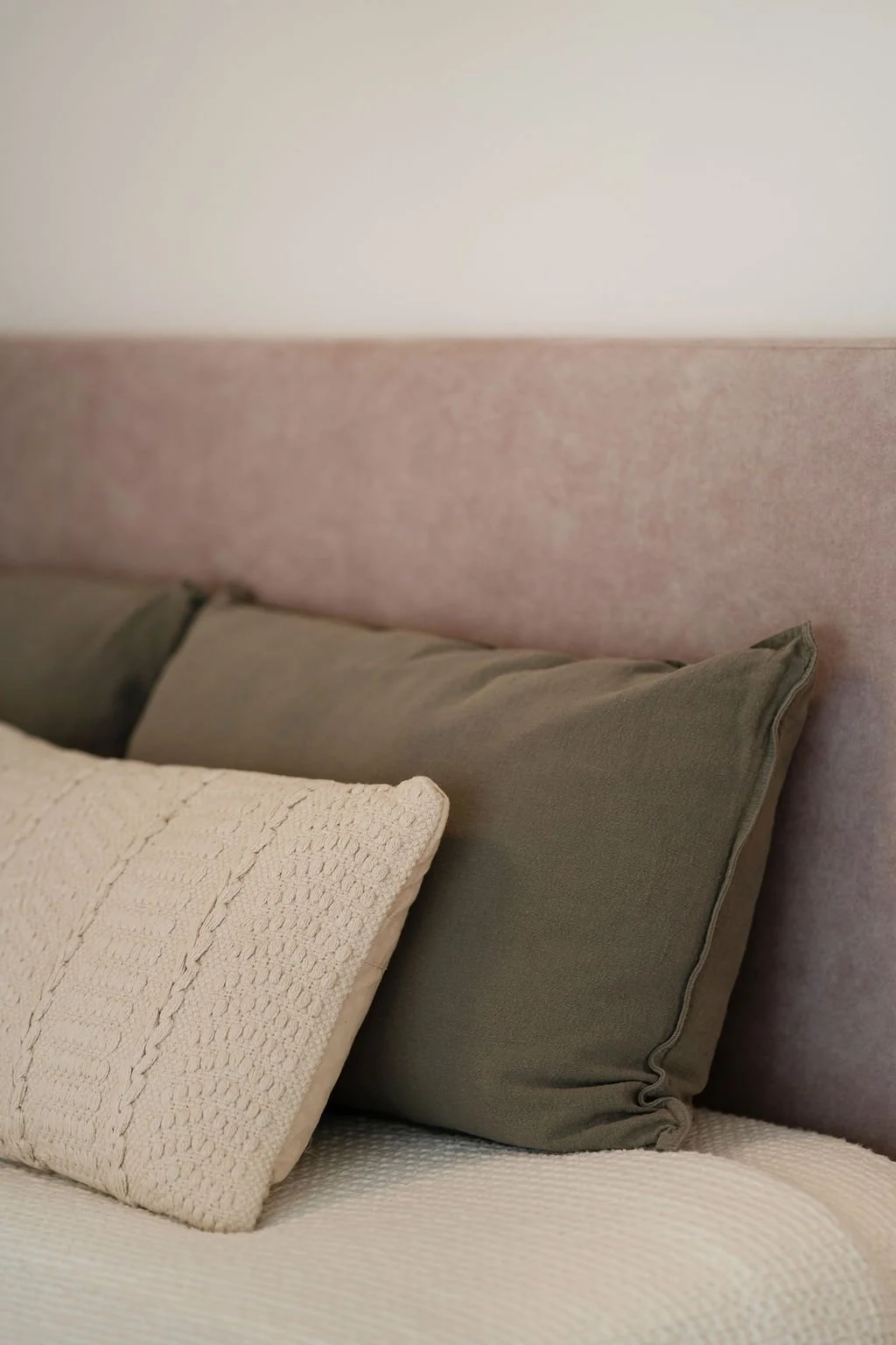 Cabeceira de cama em tecido, almofadas lisas em cor verde azeitona e almofadas texturadas acabamento crú.