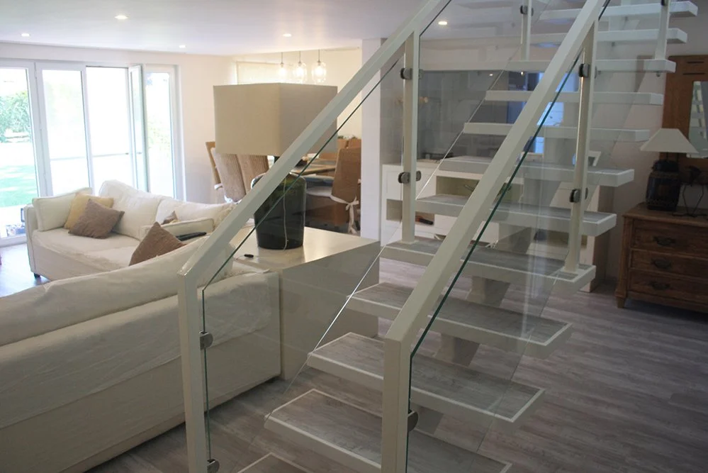 Sala de estar com sofá branco, mesinha e escada moderna de vidro e madeira.