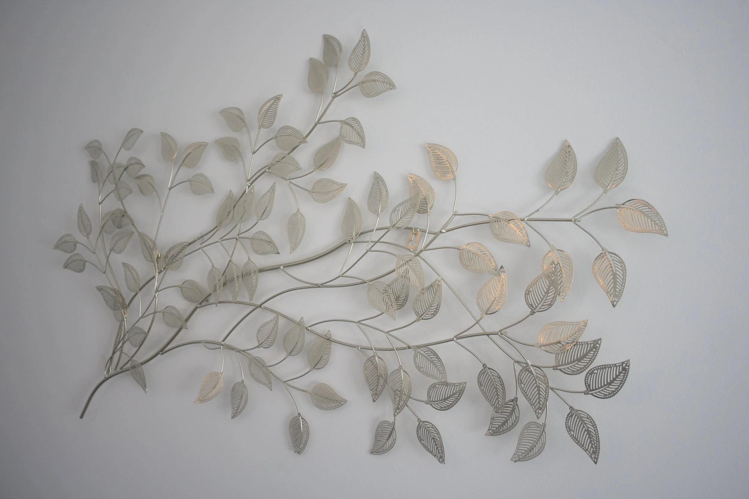 Decoração de parede com ramos de folhas metálicas douradas e prateadas.
