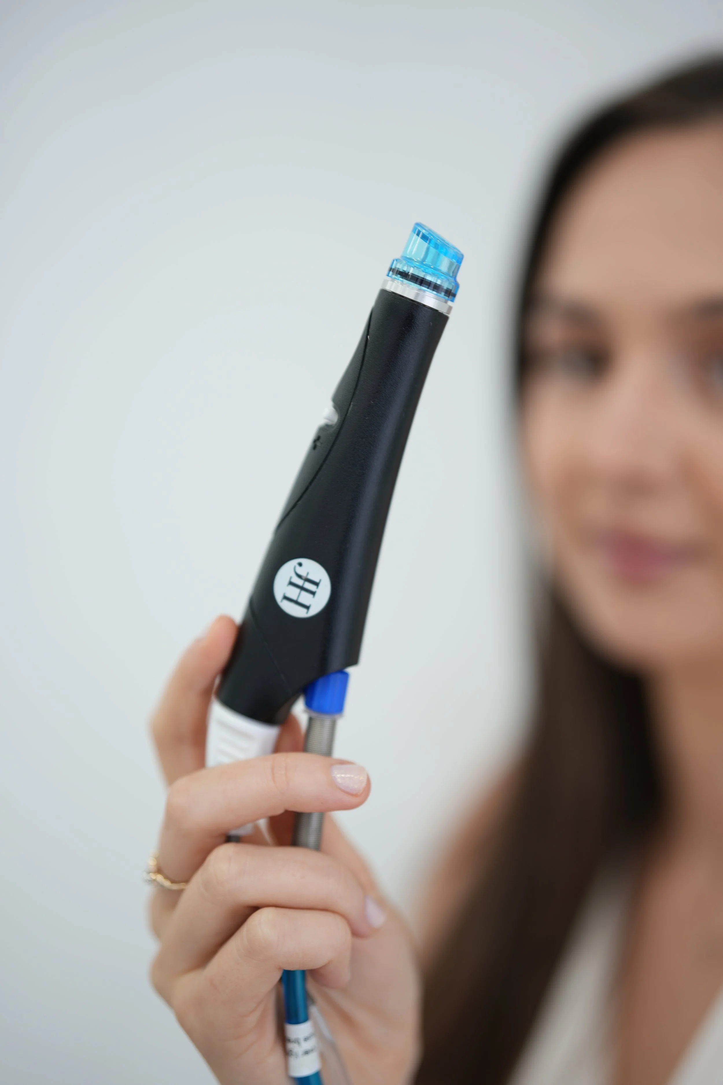 A woman holding a medical instrument, possibly a sensor device, in front of her face, with a blurred background.