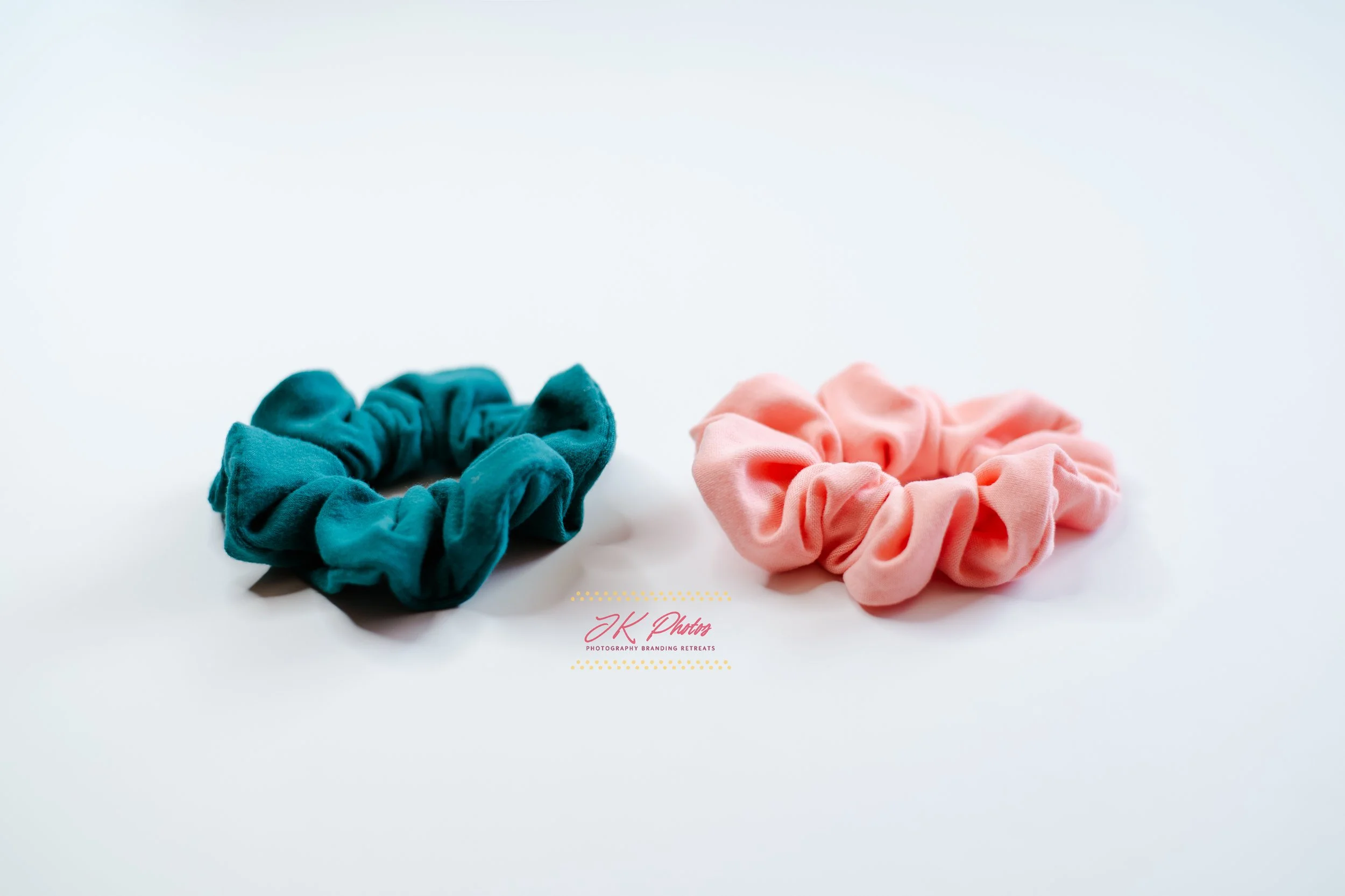 Two fabric hair scrunchies, one teal and one pink, on a white background.