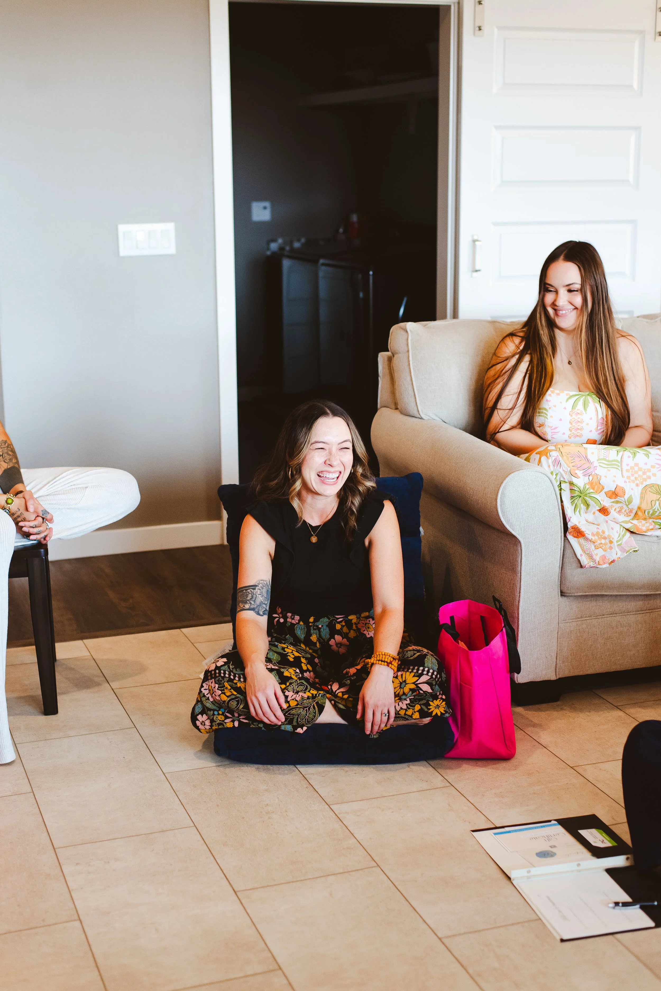Women laughing together at a retreat - one sits on the couch, the other on the floor.