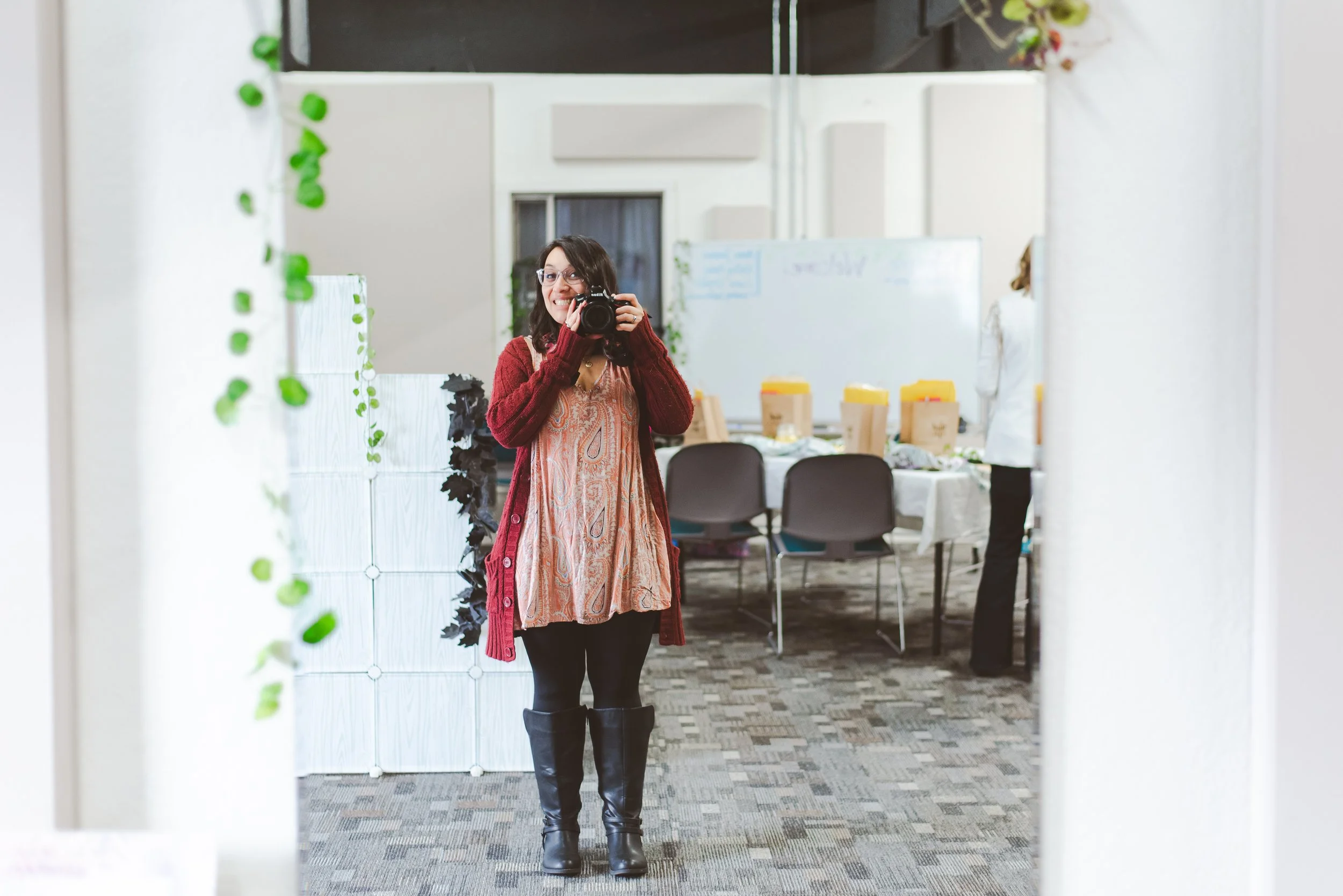 Person photographing through a mirror in a room with decorations and chairs.