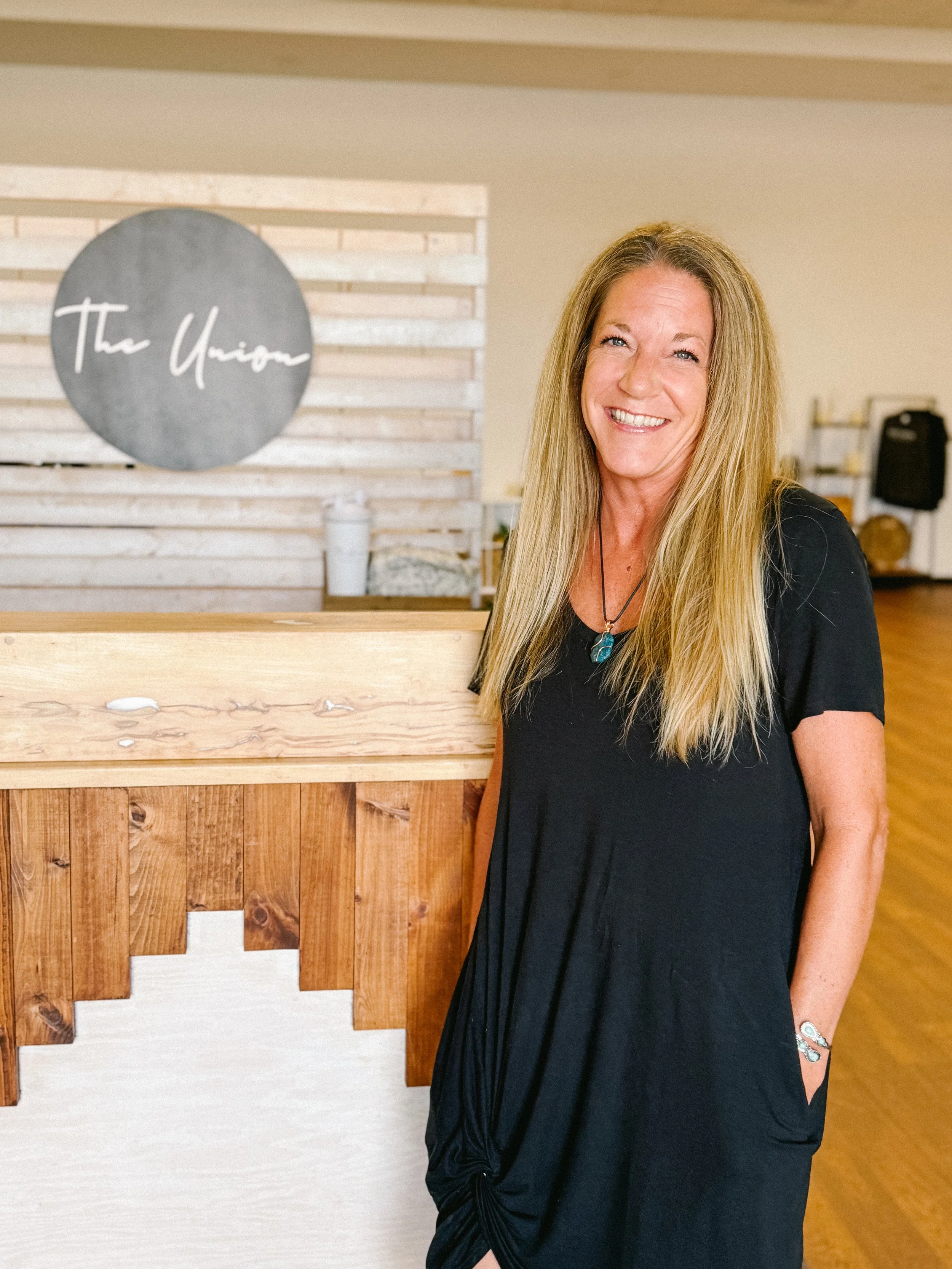 Yoga instructor, Deanna, smiles next to the front desk at The Union, Wellness Boutique.