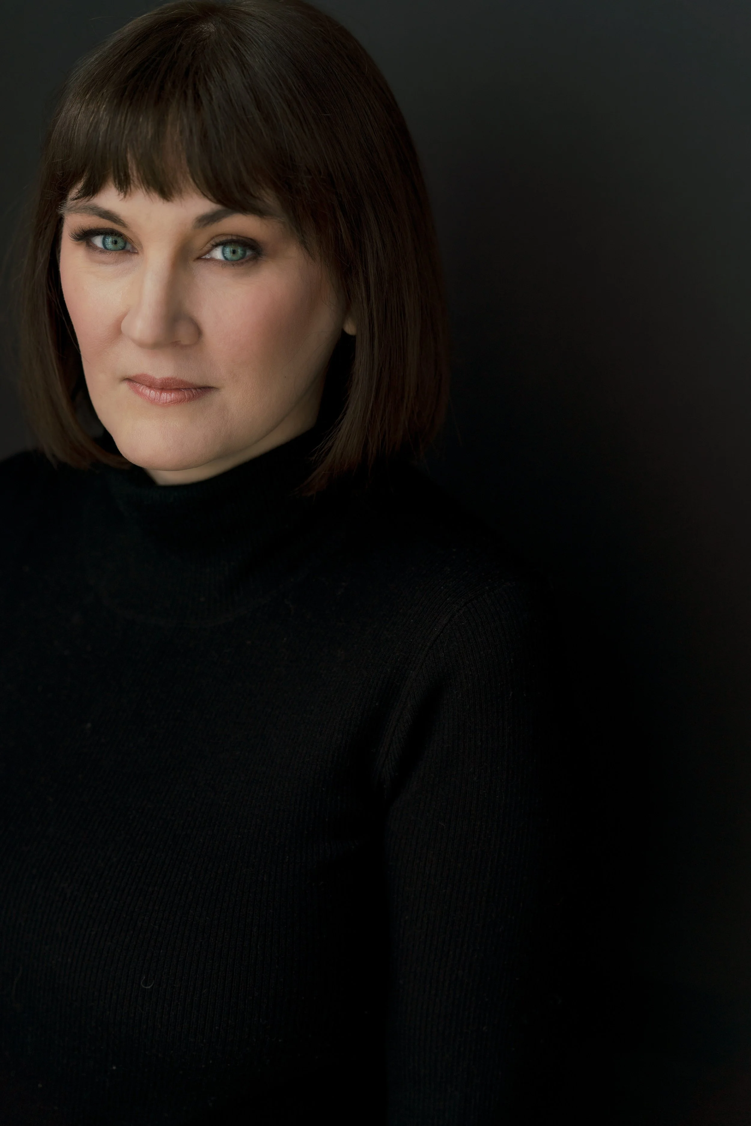 A woman looks intensely but stoic in a headshot portrait against a black background. She pops from the backdrop and is left aligned for her professional portrait.