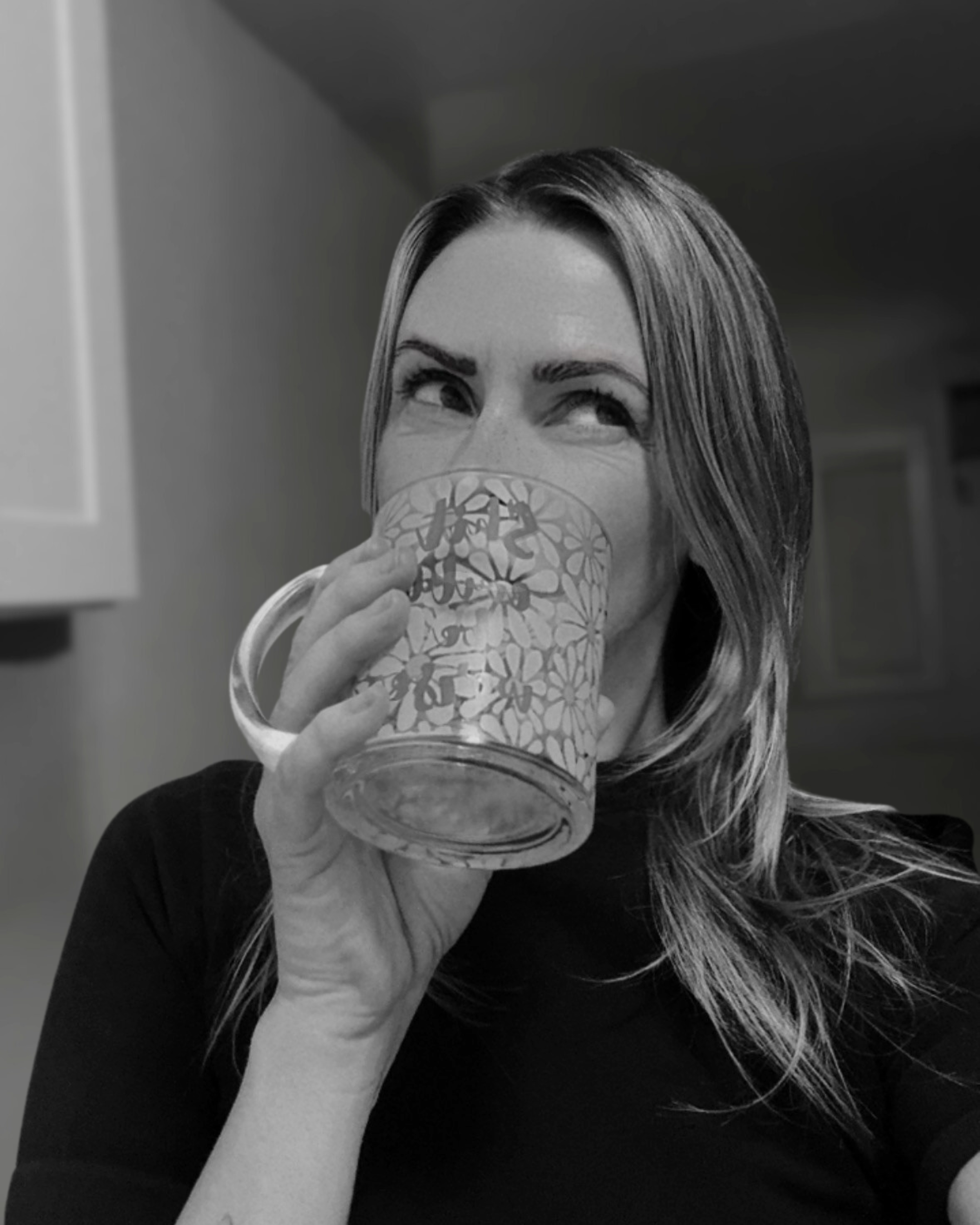 Woman drinking out of a glass coffee mug, looking skeptical