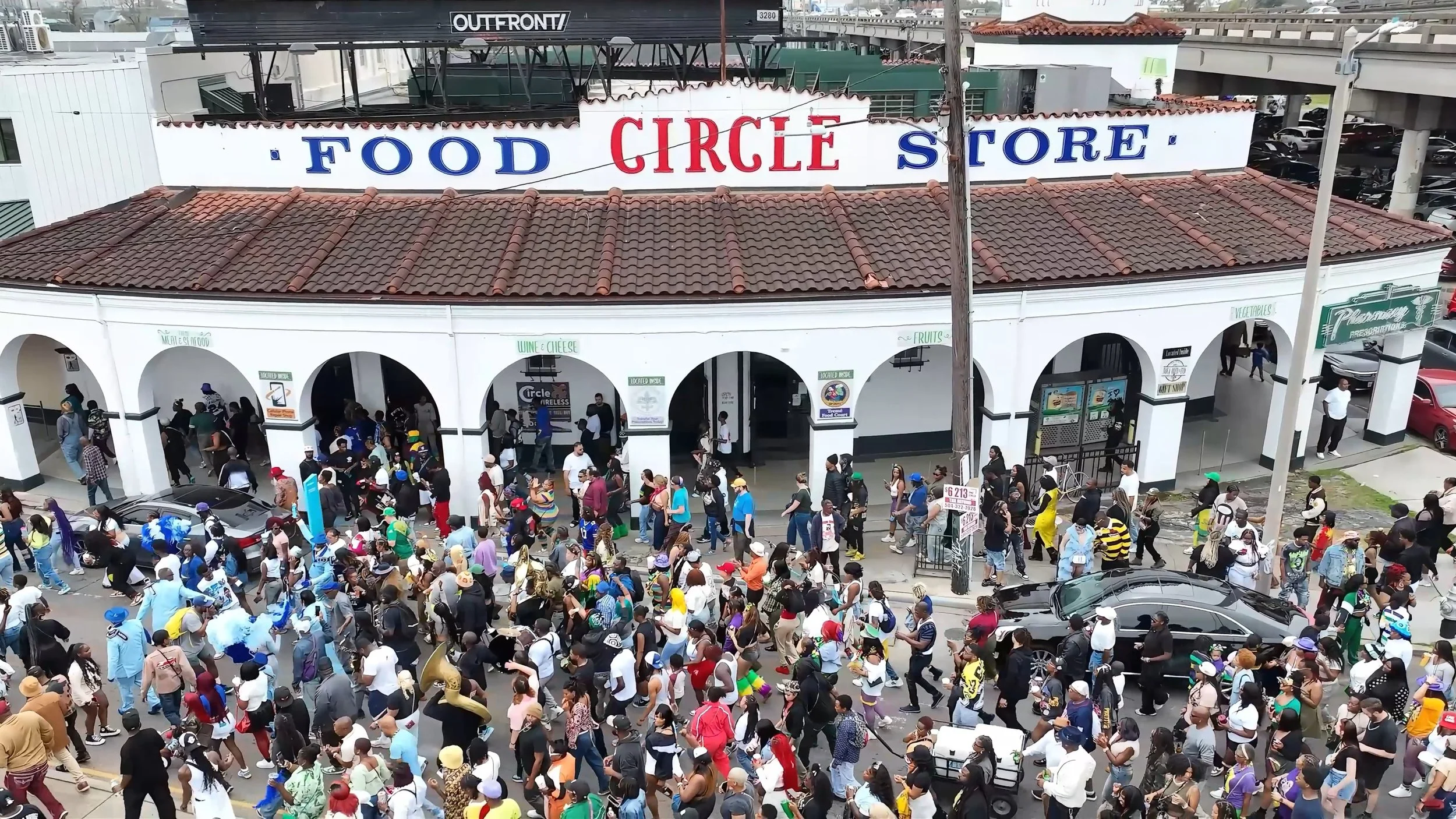 Crowd of people in colorful costumes and hats walking past a food store named Circle, in a bustling city street.