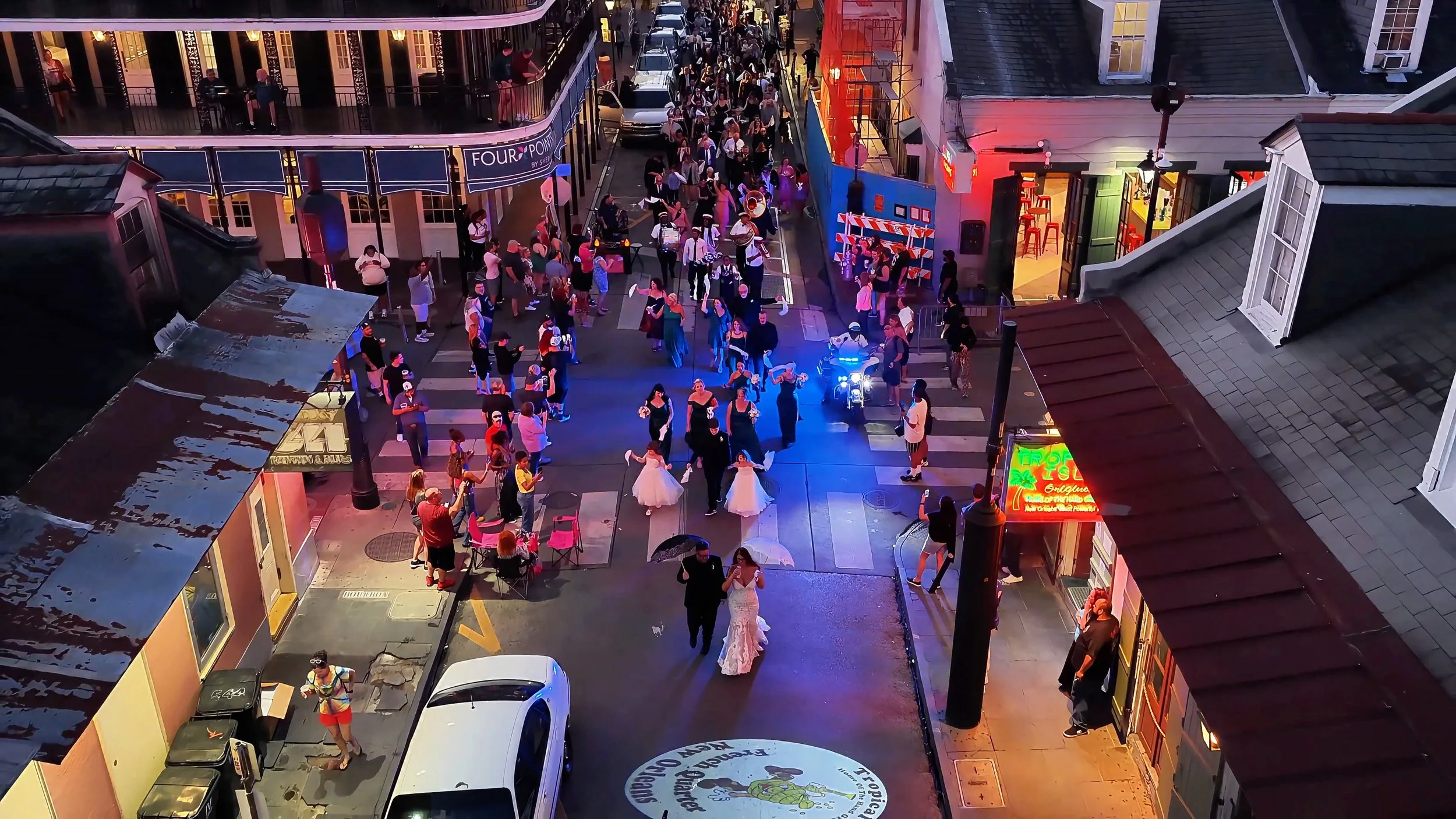 A lively street scene during a nighttime celebration with people dancing, some holding umbrellas, and enjoying the festive atmosphere surrounded by buildings with neon signs and lights.