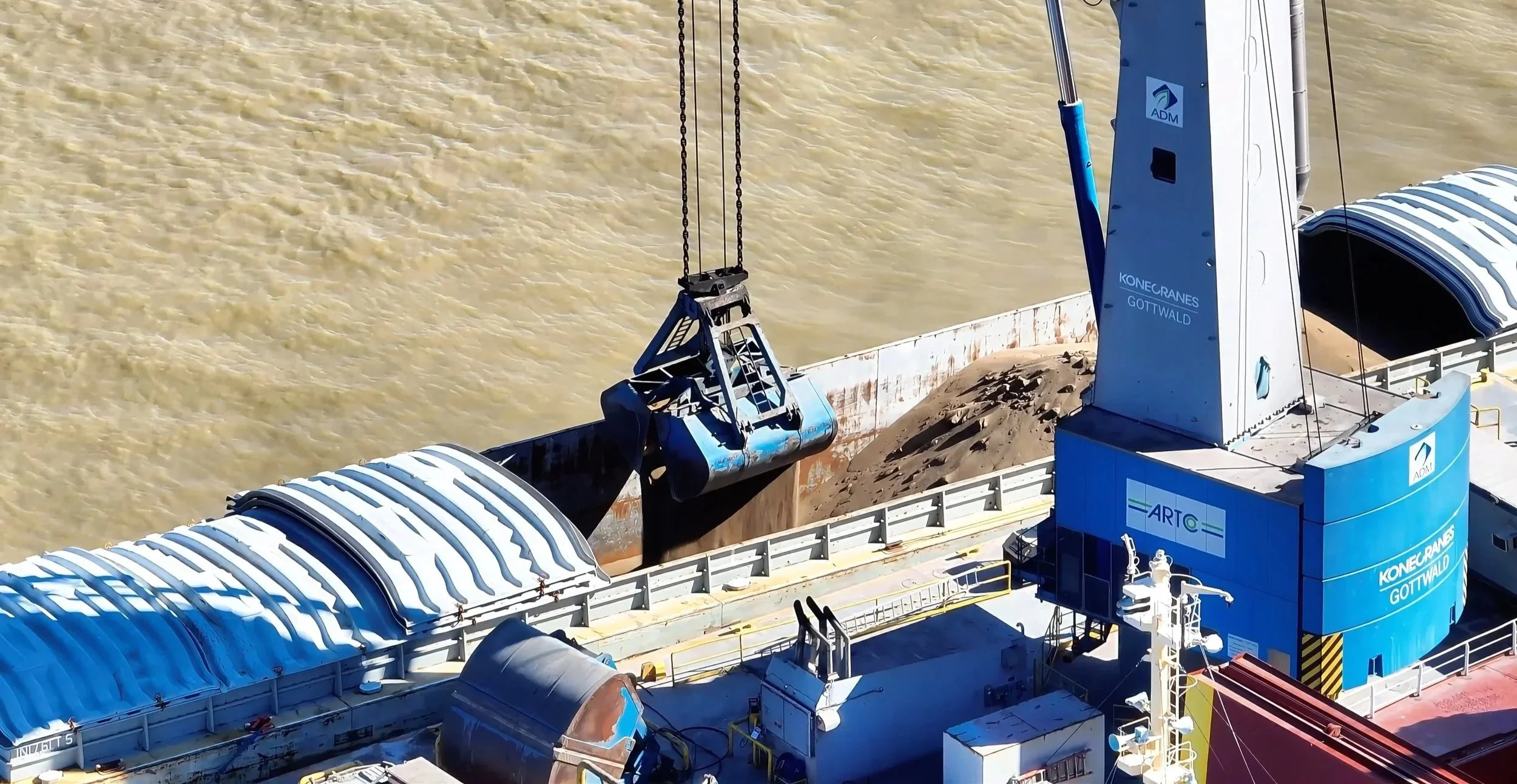 A large blue dredging machine on a waterway with muddy water in the background, lifting a bucket of sediment from the riverbed.