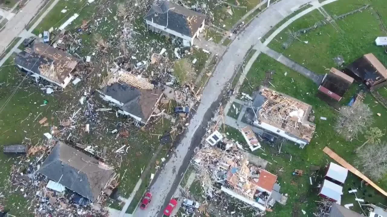 Aerial view of a neighborhood showing several houses severely damaged from a tornado, with debris scattered across the yards and streets.