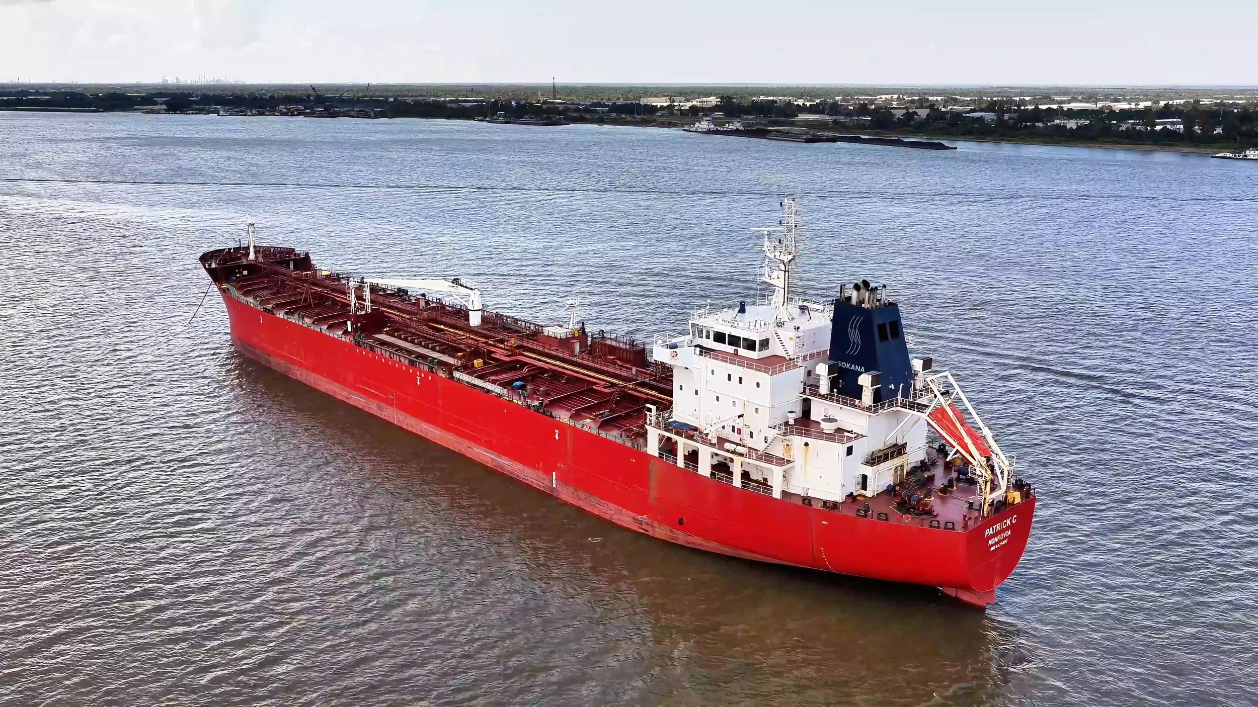 A large red tanker ship sailing in a body of water near a coastline.