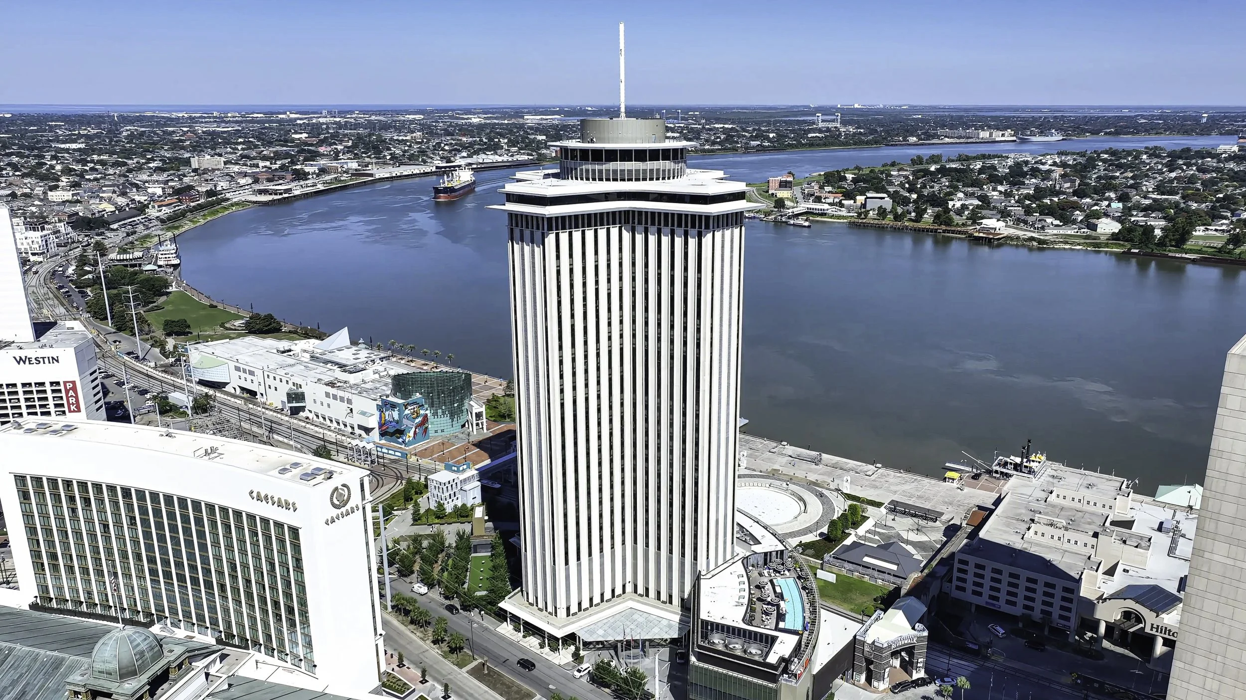 A high-rise building with vertical white stripes located near a river, surrounded by other buildings and city infrastructure.