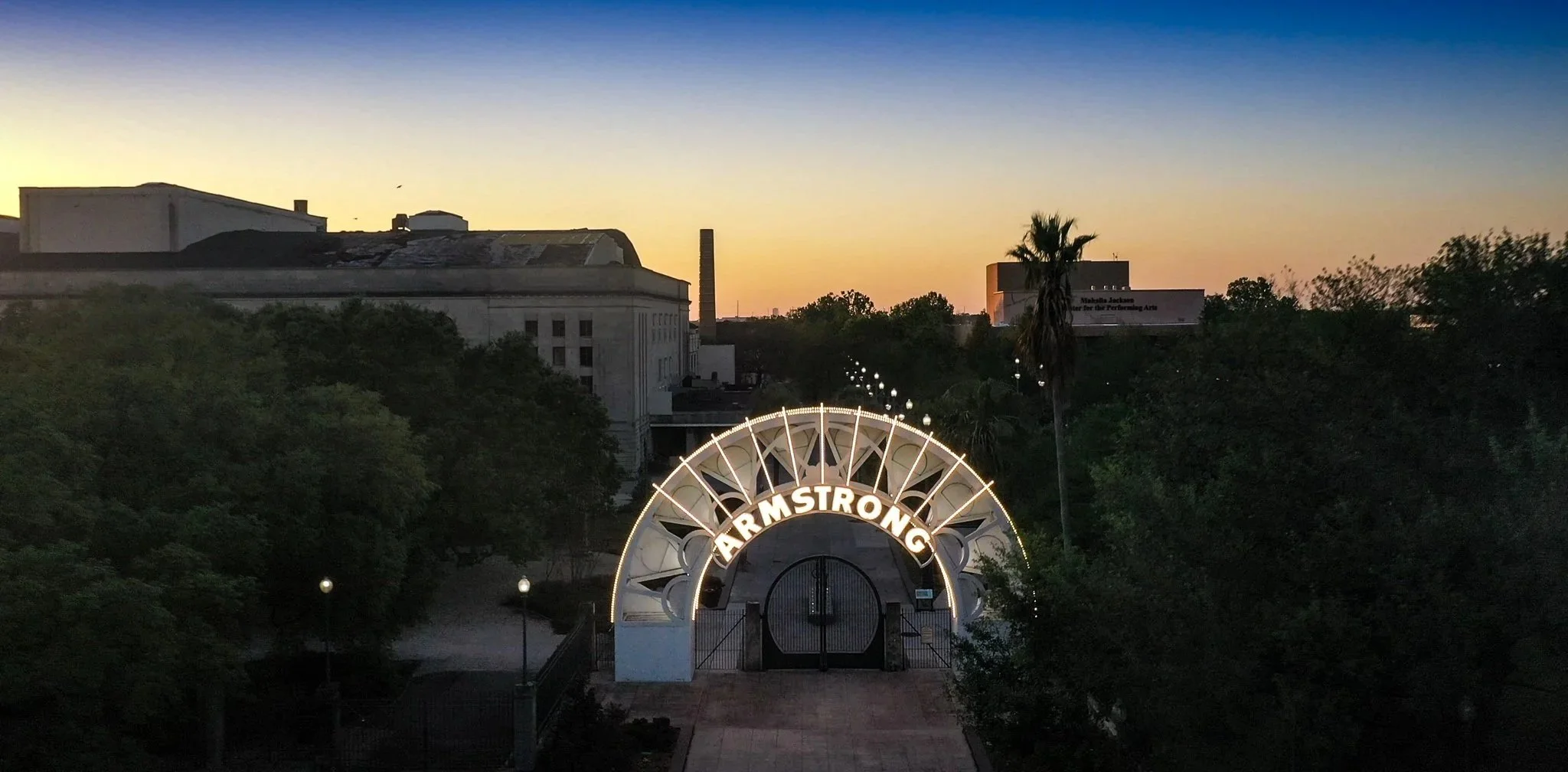 Sunset sky over the Armstrong building entrance in Houston, Texas, with trees and street lamps in the foreground.