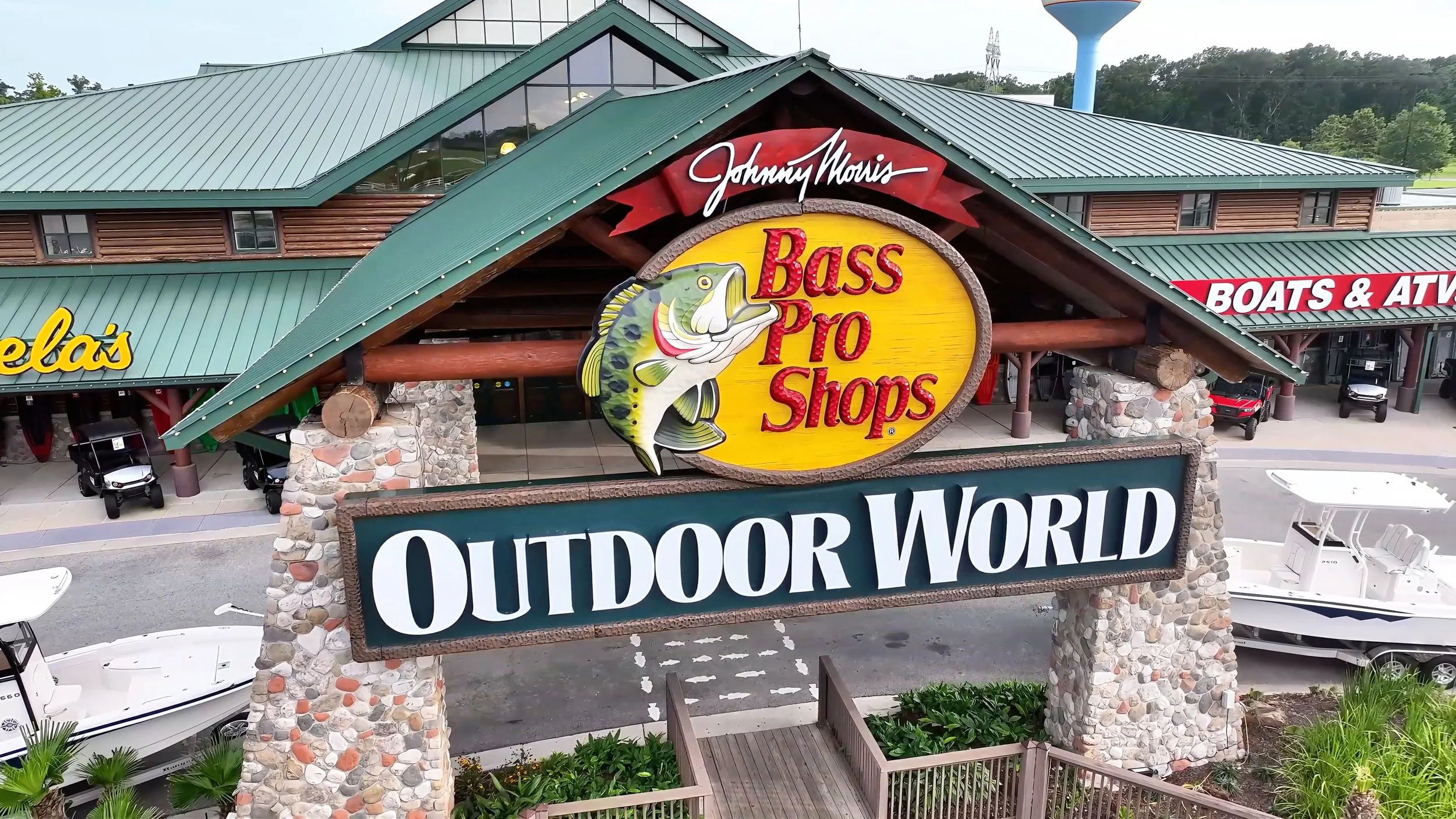 Sign for Johnny Morris Bass Pro Shops Outdoor World surrounded by boats and outdoor equipment at the store entrance.