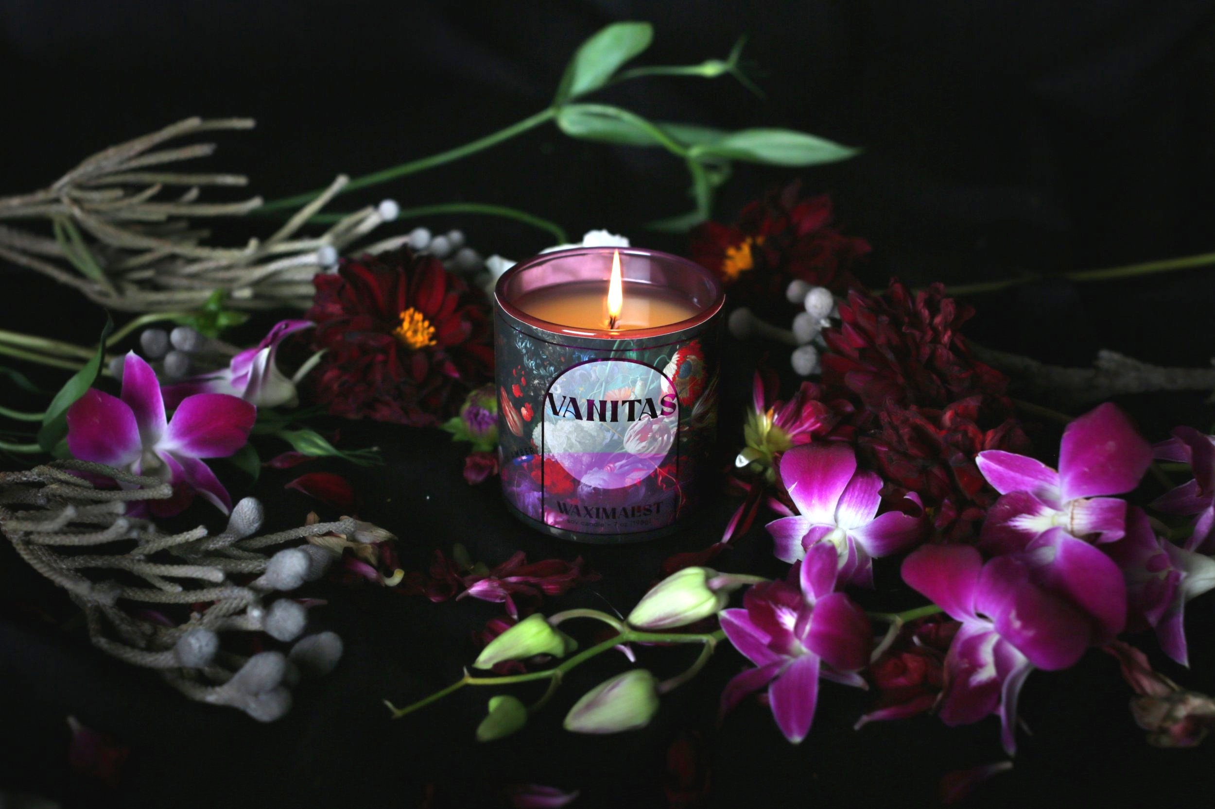 Image of candle with purple metallic floral label sitting among orchids and other flowers