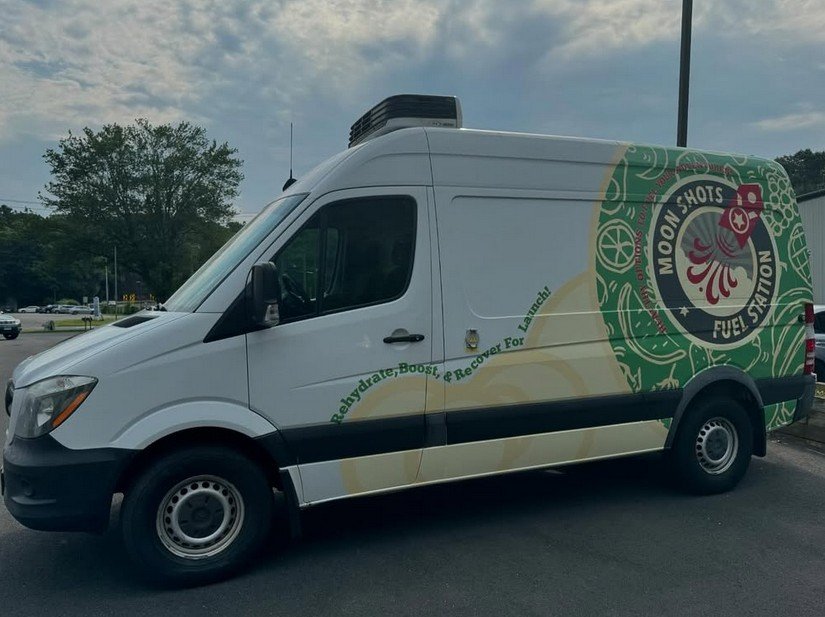 White van with side graphics promoting Moon Shots Fuel Station and featuring colorful designs and text about renewable, boost, and recovery energy.