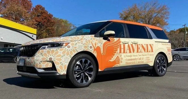 A vehicle with a beige and orange design featuring a phoenix and the word "HAVENLY" on its side, parked in a parking lot.