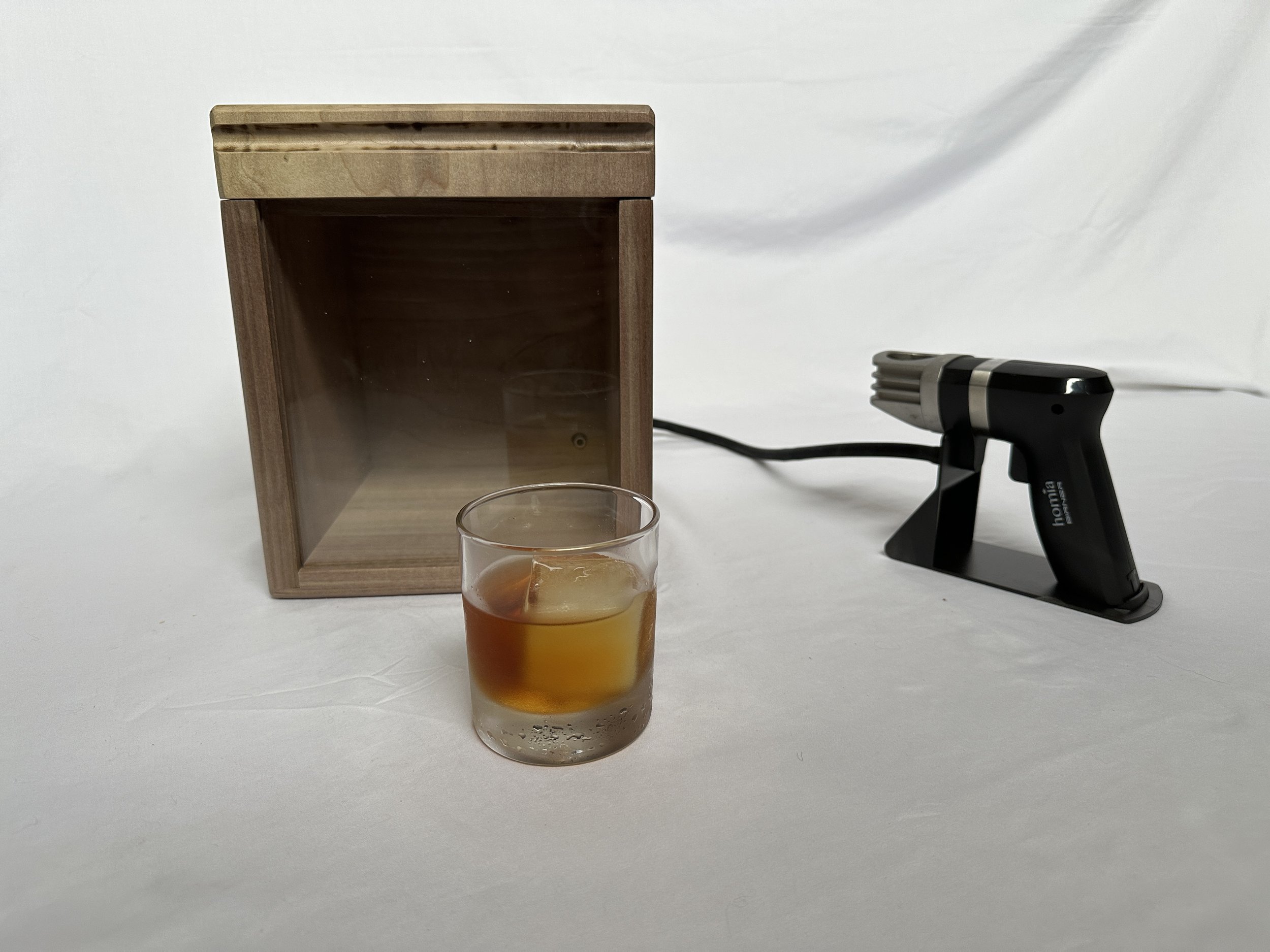 Rail Cocktail Smoker Box in natural wood with an Old Fashioned cocktail and Homia smoke infuser gun - handcrafted smoker box by CARLYWOOD Creations used fo clear glass with a layered beverage, a wooden box, a white backdrop, and a black hair trimmer.