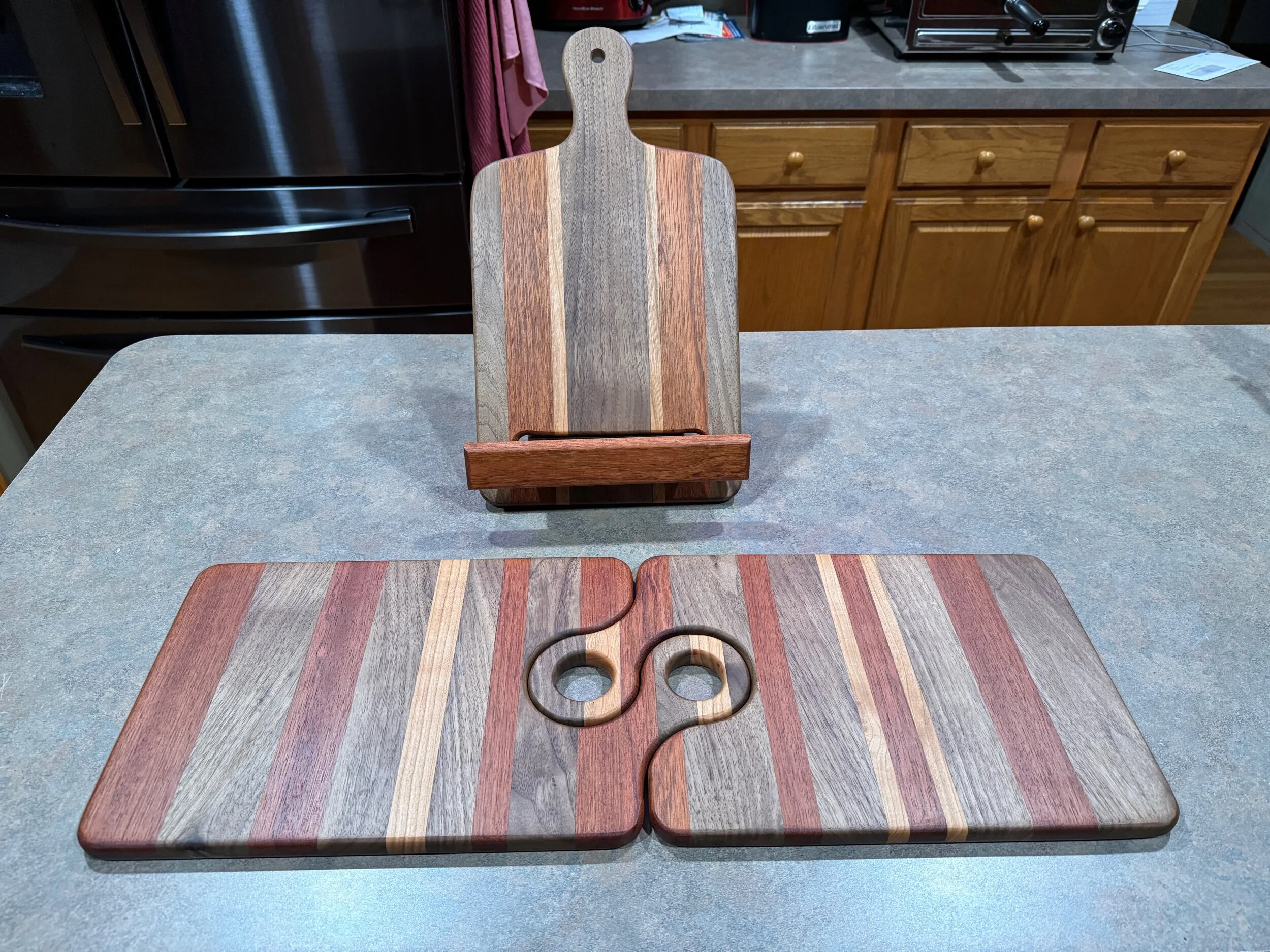 A set of Three wooden items. 1 receipt stand and 2 charcuterie boards, all with striped patterns and a similar coloring.