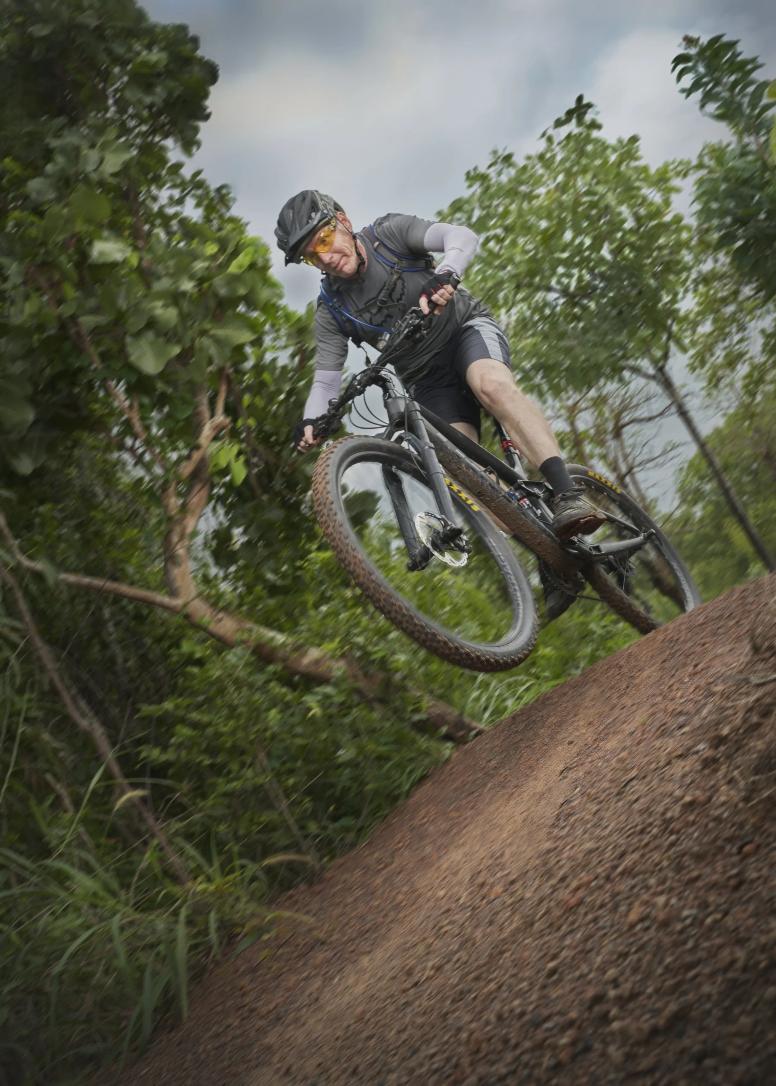 A man in cycling gear navigating a steep dirt trail on a mountain bike in a forest.