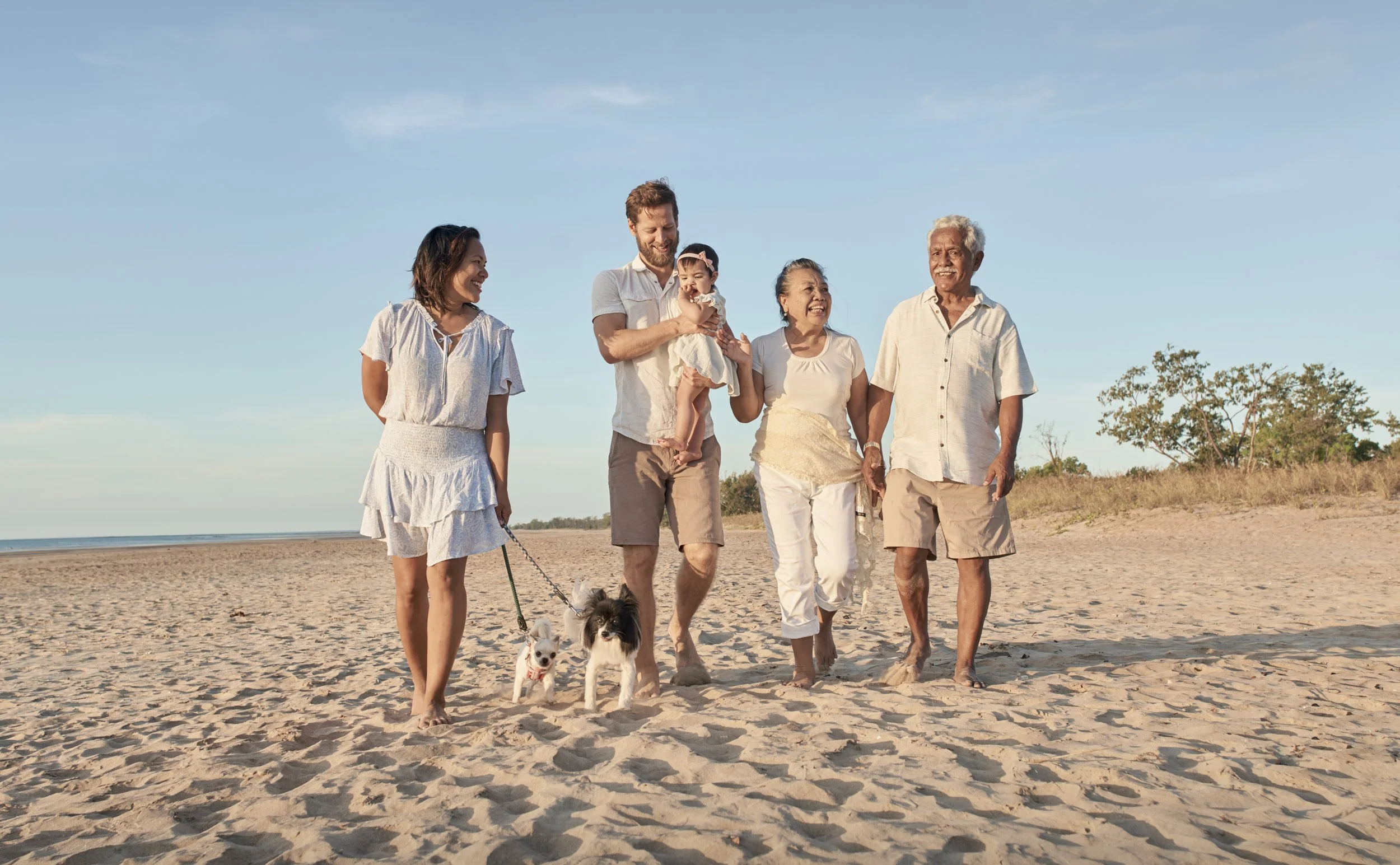 Multi-generational family walking on the beach with dogs