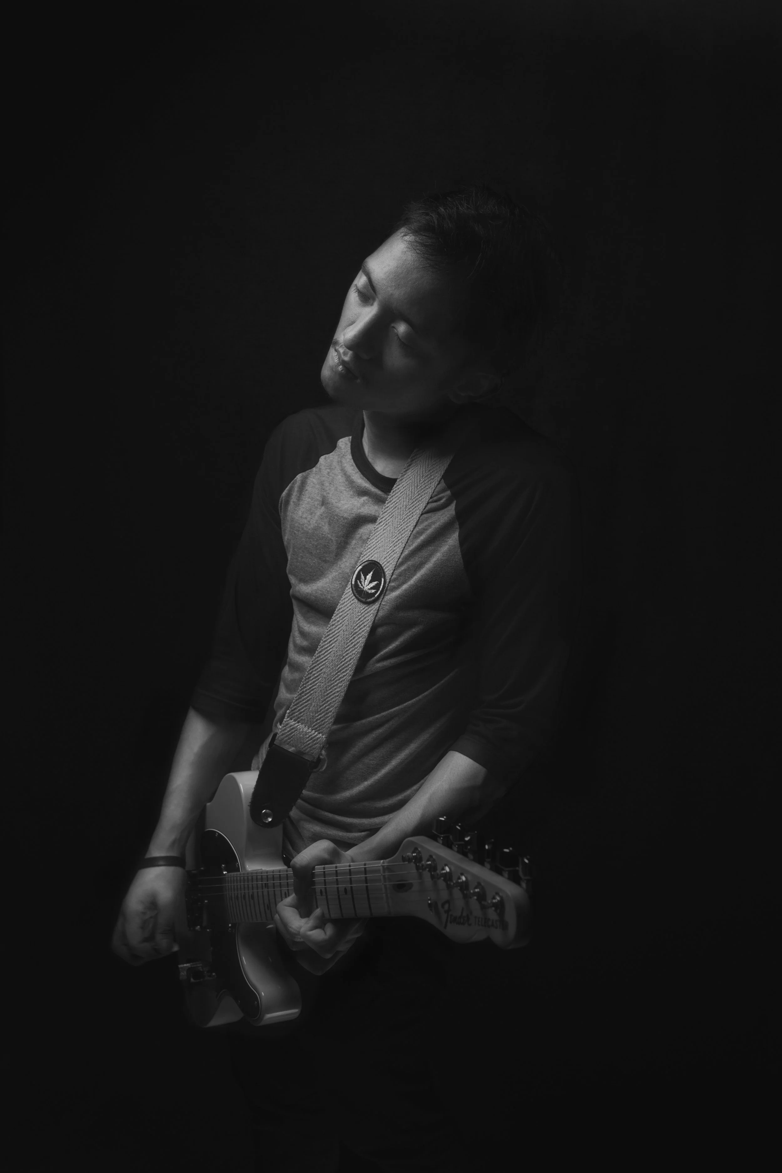 A young man playing an electric guitar in a dark setting, with a focused expression and eyes closed.