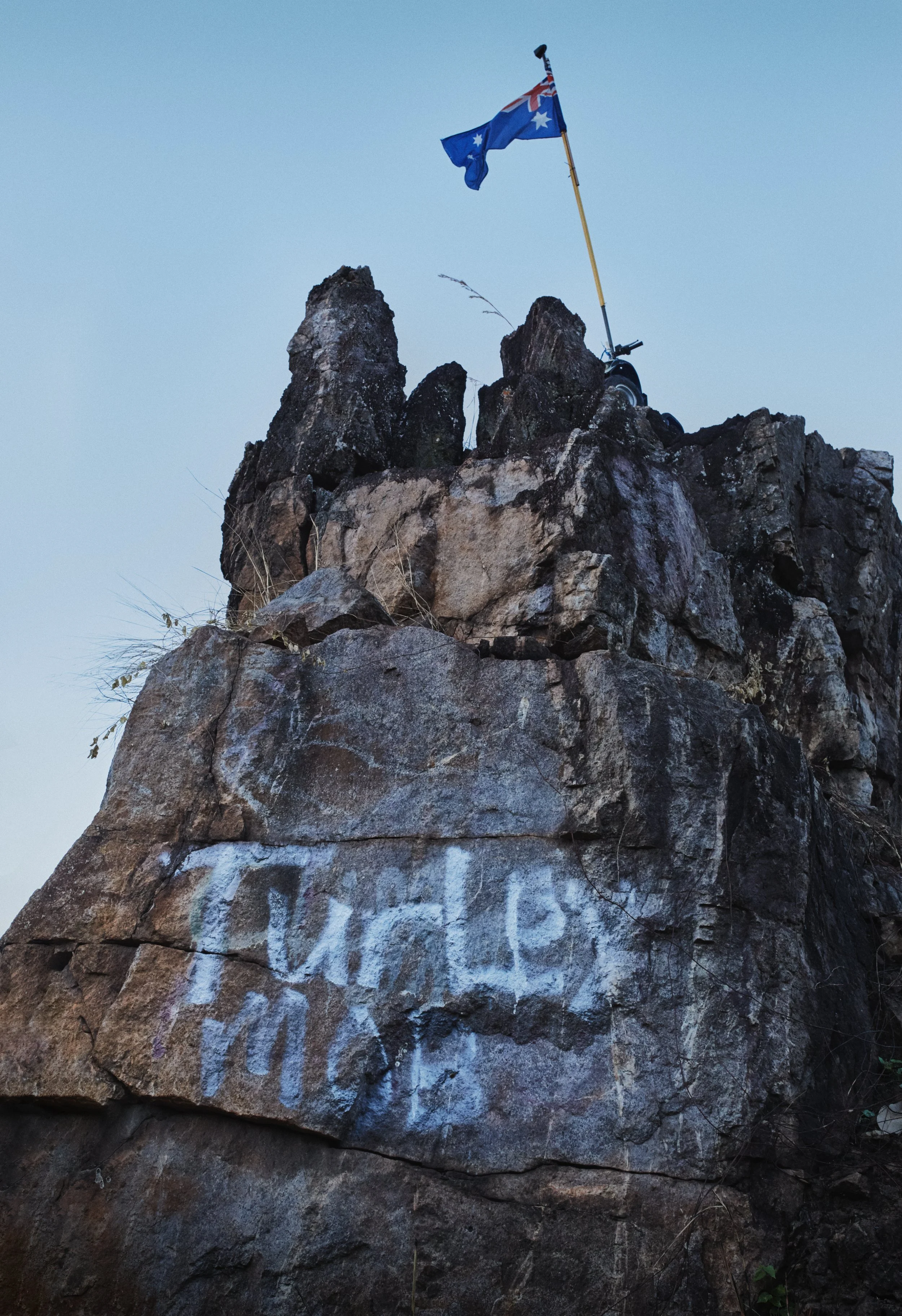 A rock formation with a blue Australian flag on top. The rock has white graffiti on it.