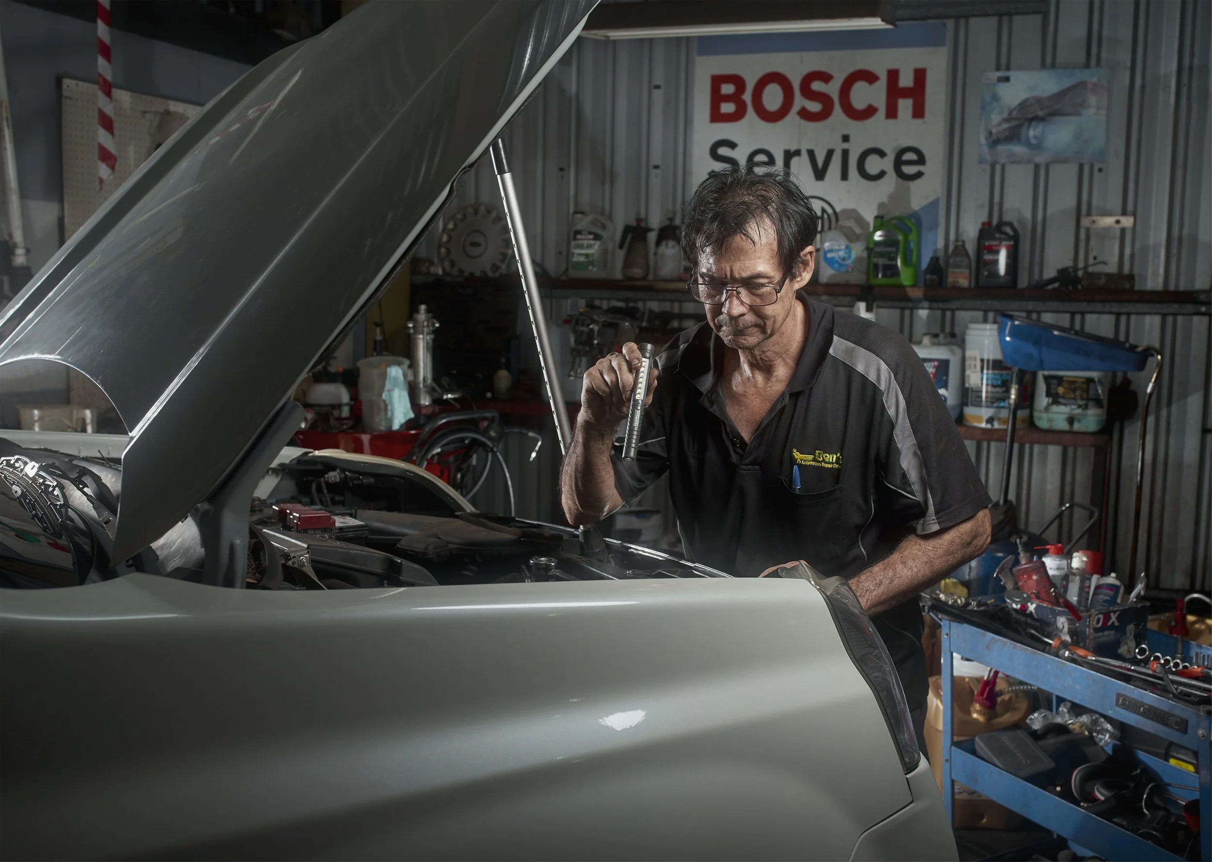 A mechanic working on a car engine in an auto repair shop with a Bosch Service sign in the background.