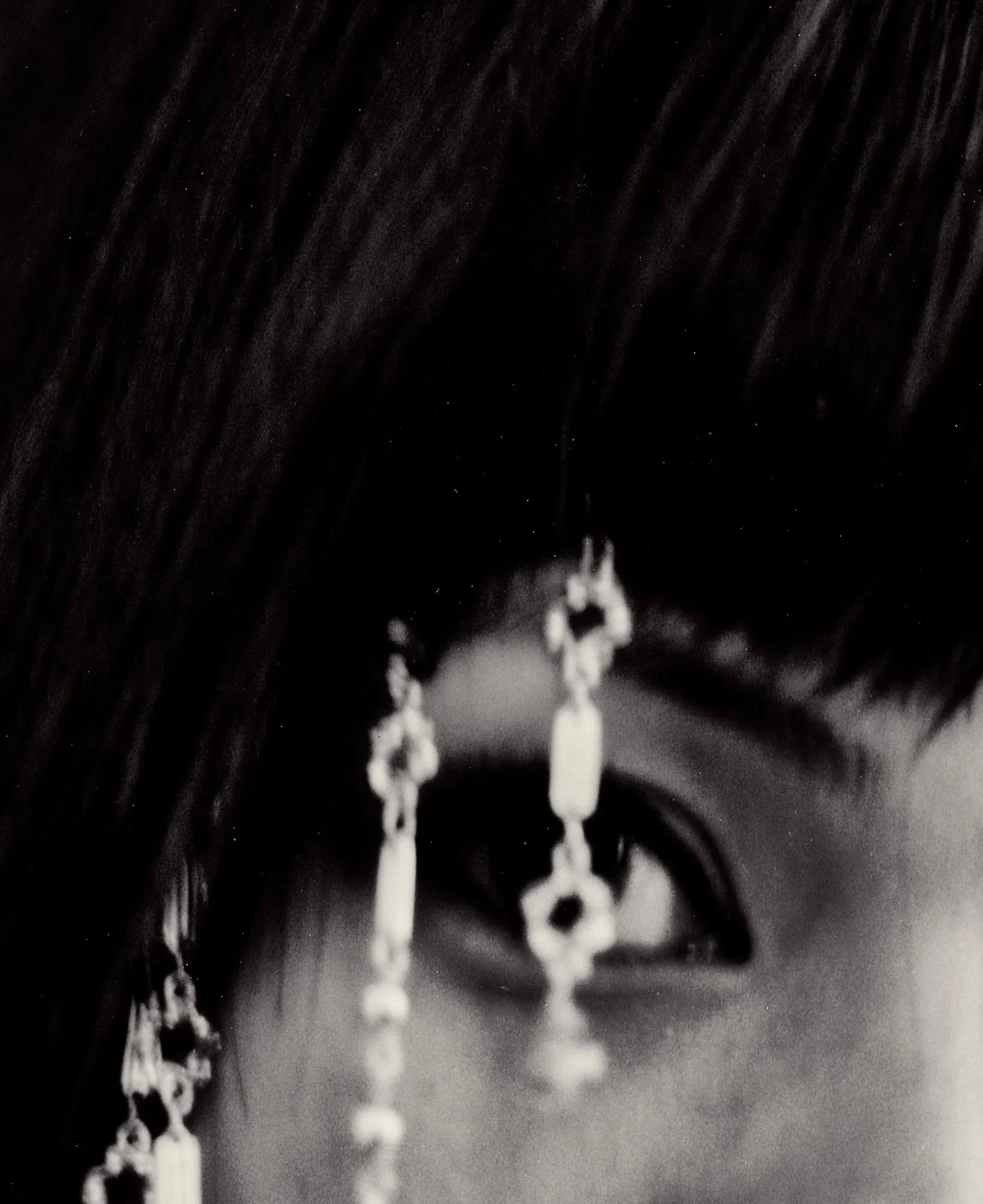Close-up of a necklace chain with small, round beads and a pendant, displayed against a dark background.