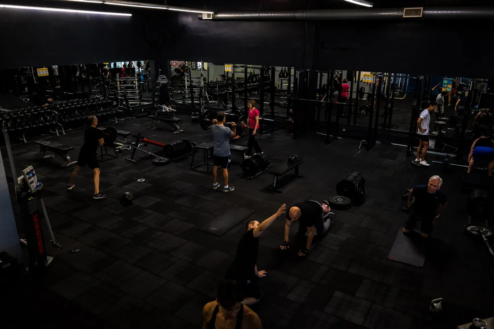 the gym floor from above, members training among racks, benches and free weights