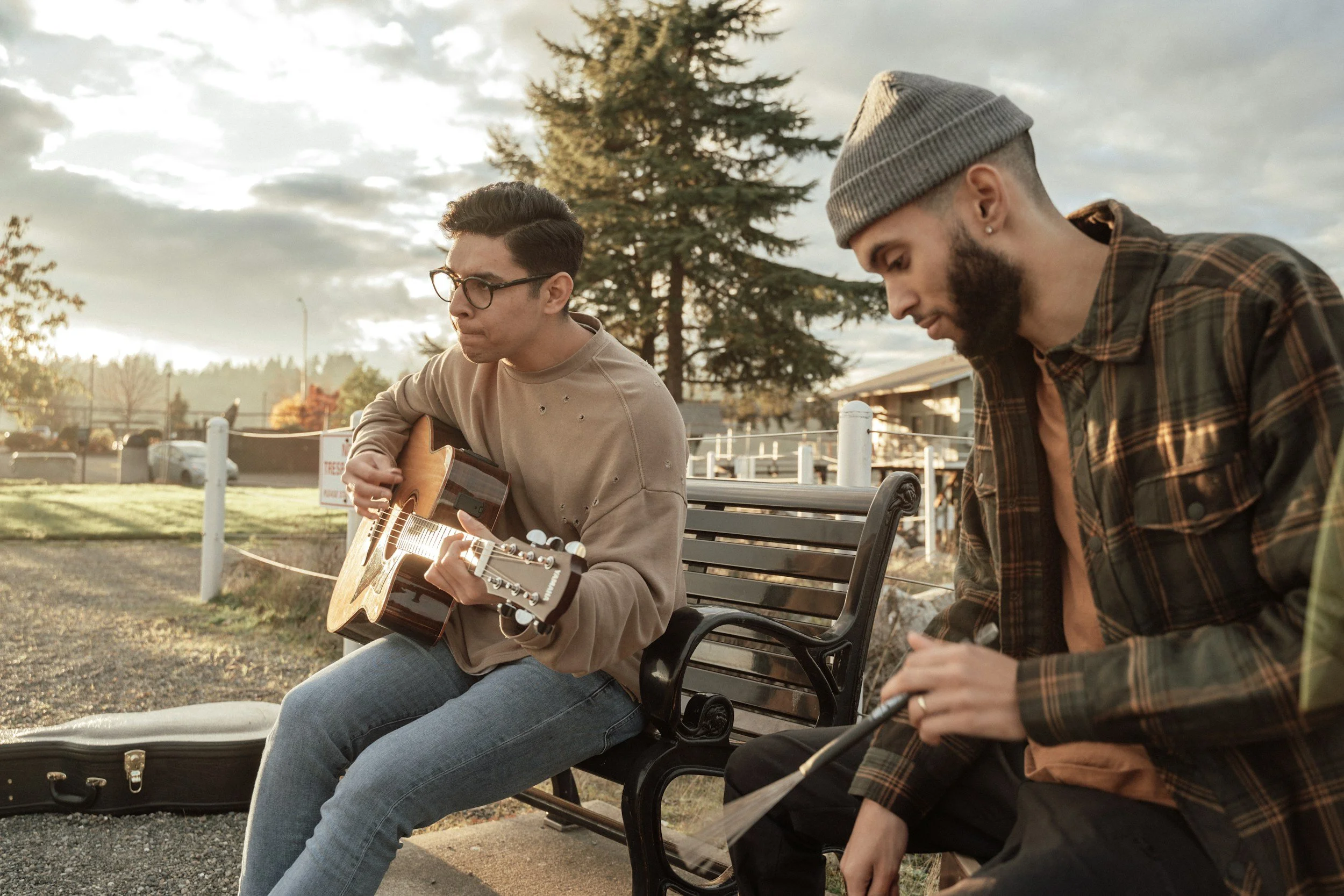 Two musicians sitting on a bench talking, one holding an acoustic guitar
