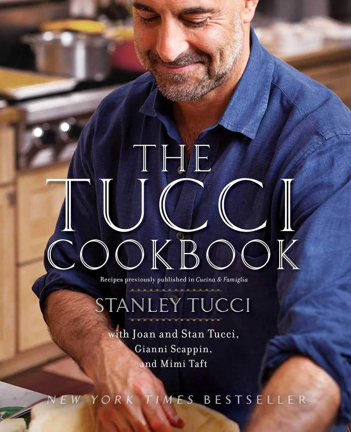 Cover of The Tucci Cookbook featuring a smiling man with gray hair and beard in a blue shirt, in a kitchen.