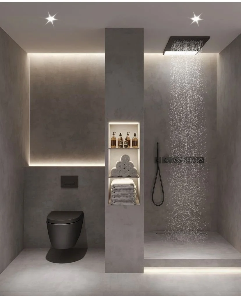 Modern bathroom with a toilet, a shower area with rain shower head, and minimalist storage with towels and soap bottles, all in a sleek, gray, concrete-style finish.