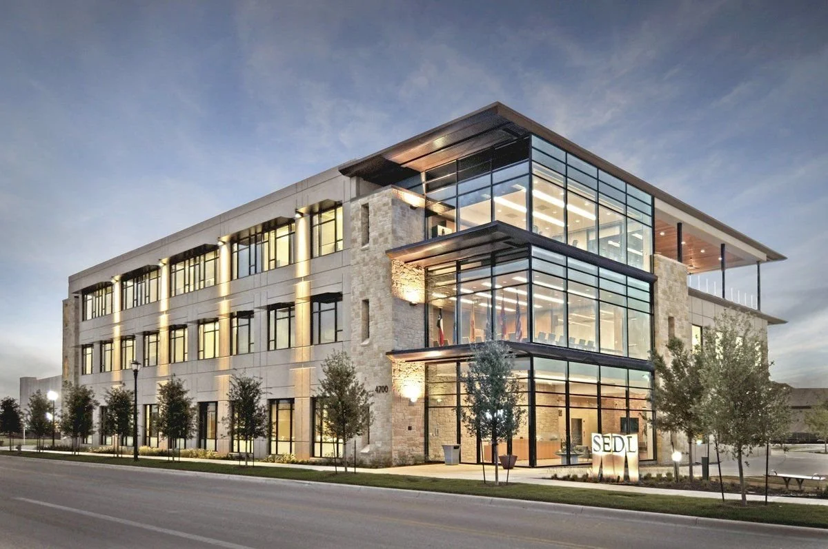 Modern, multi-story office building with glass windows and trees in front at dusk.