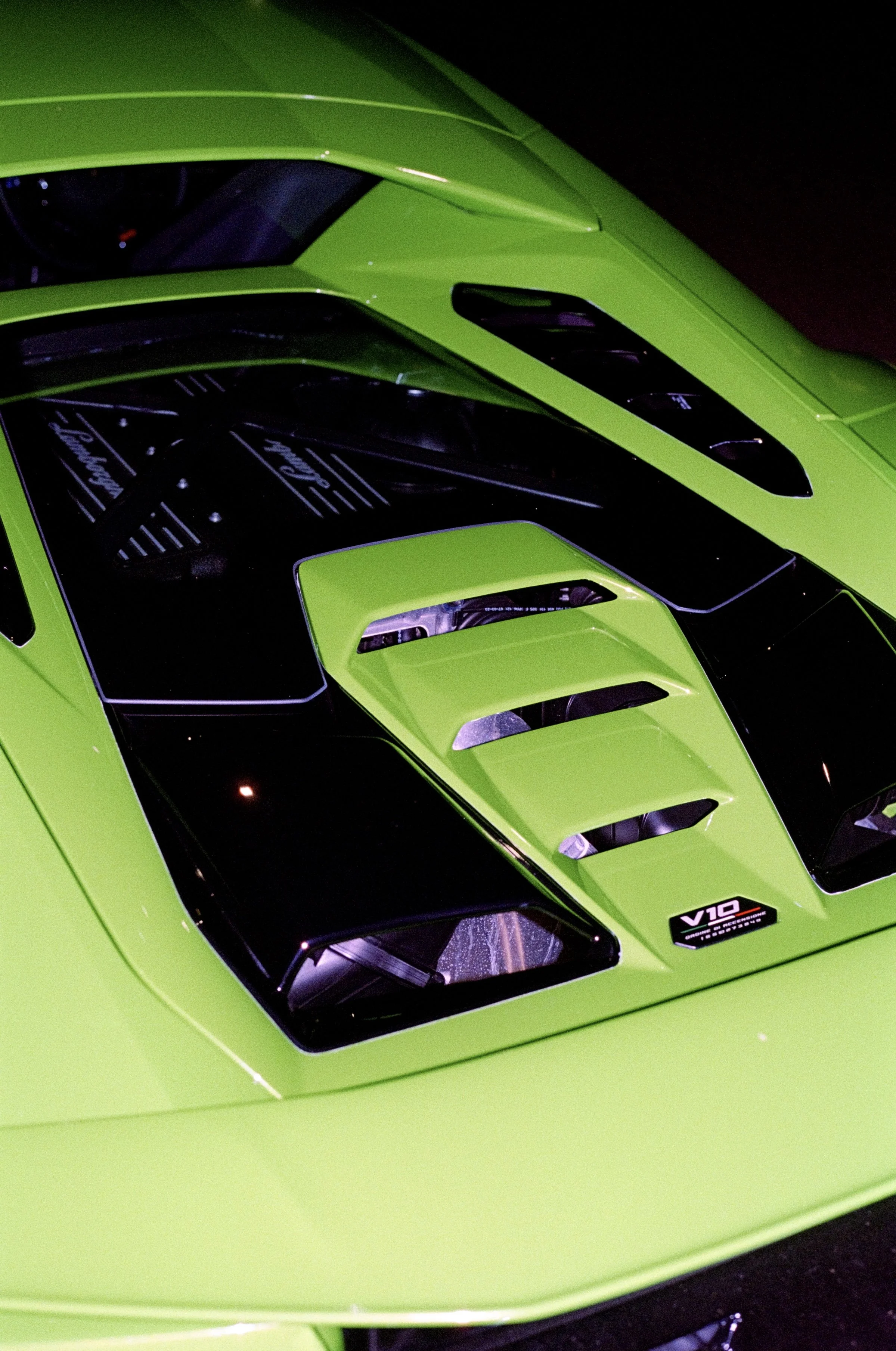 Close-up of a bright green sports car with black accents, showing the front and part of the windshield, with a sticker on the windshield indicating a V10 engine.