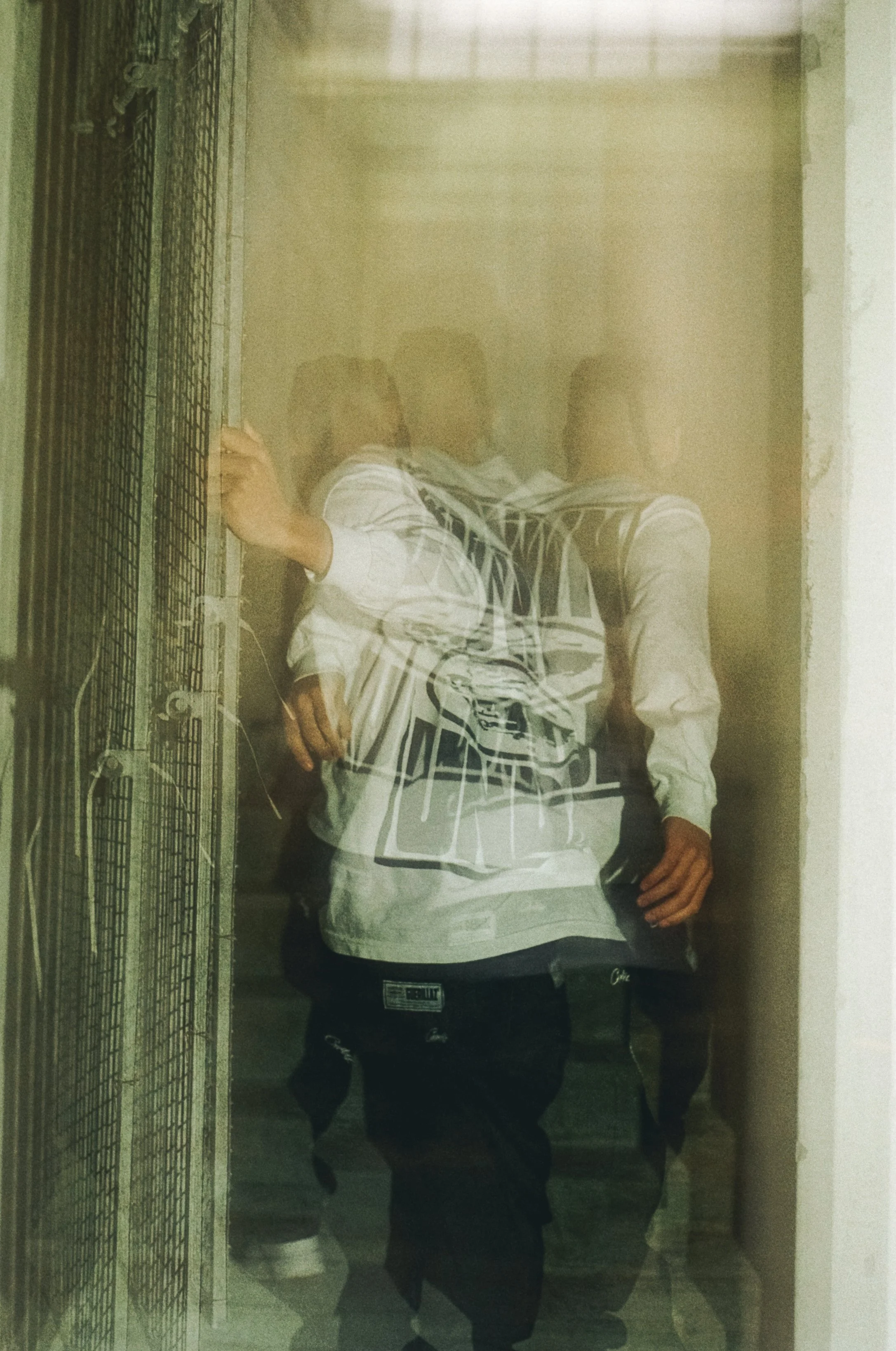 Person standing in front of a mirror, taking a photo with a phone, wearing a white and black striped hoodie and black pants, with a wire cage to the side.