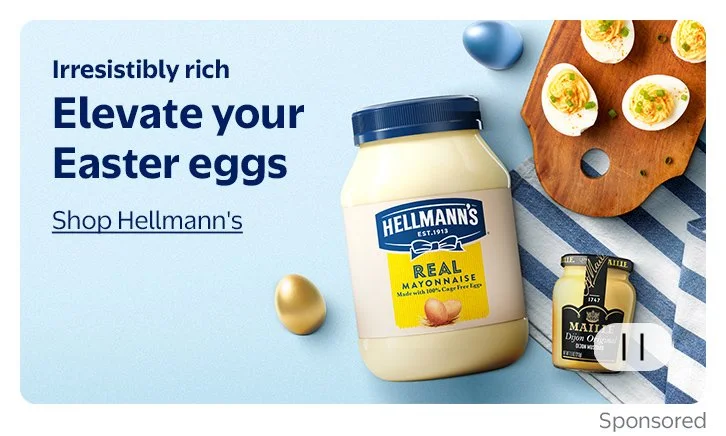 A Hellomann's jar of mayonnaise, a small bottle of Dijon mustard, and a wooden board with halved Easter eggs topped with herbs, set on a blue and white striped napkin with colorful eggs around, on a light blue background. Text reads 'Irresistibly rich, Elevate your Easter eggs, Shop Hellmann's'.