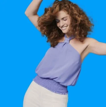 Young woman with curly hair smiling and dancing against a bright blue background.