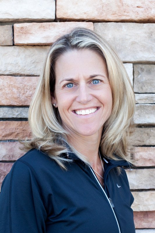 A tattooed woman wearing a white cap and gray tank top with the word 'REFUGE' on it, raising her right arm in a gym-like setting with a dark green curtain background.